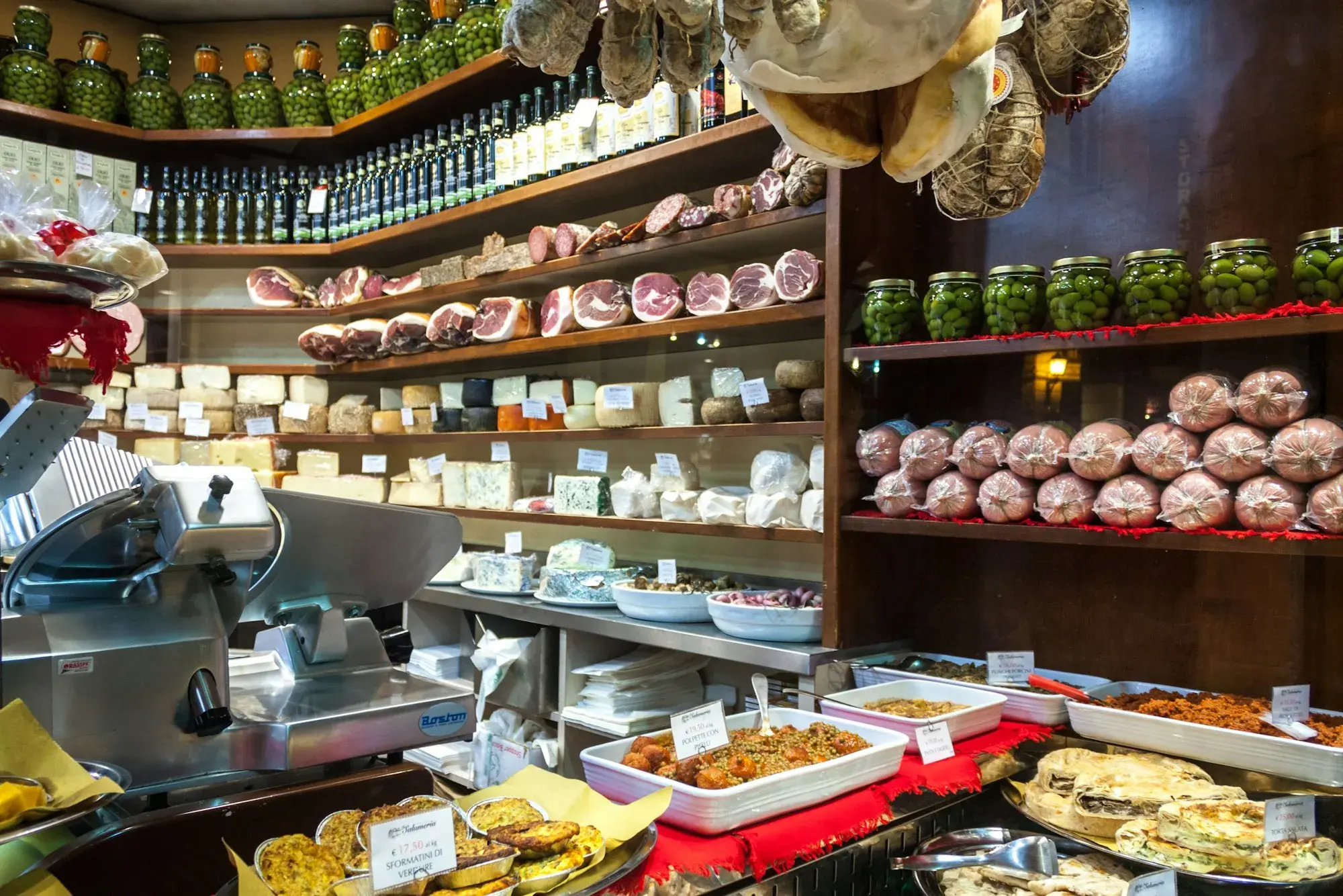Inside a delicatessen in Bologna, with shelves and counters full of cheeses, cured meats, olives and prepared dishes
