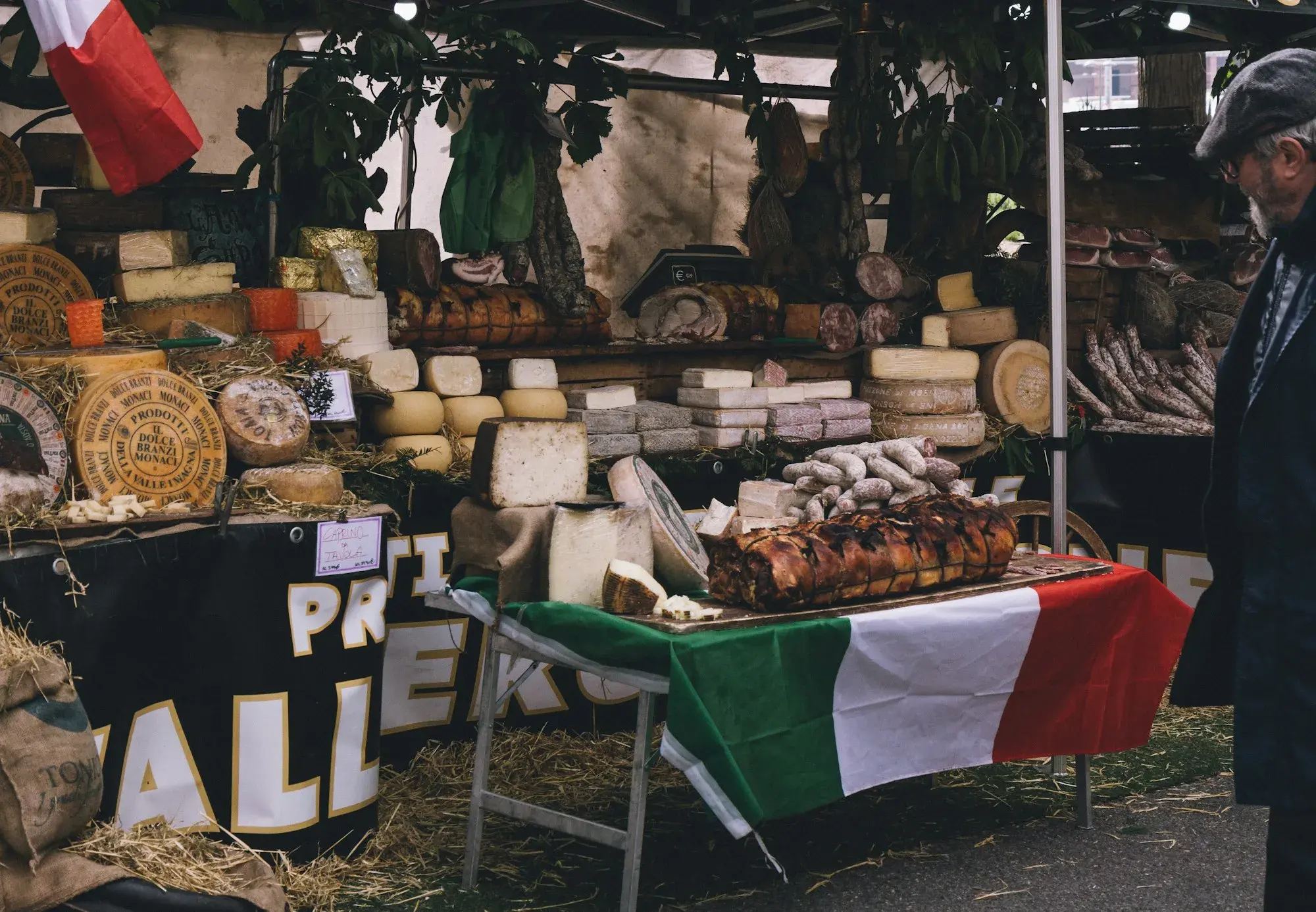 A market stall in Bologna with wheels and wedges of cheese, hams and an Italian flag