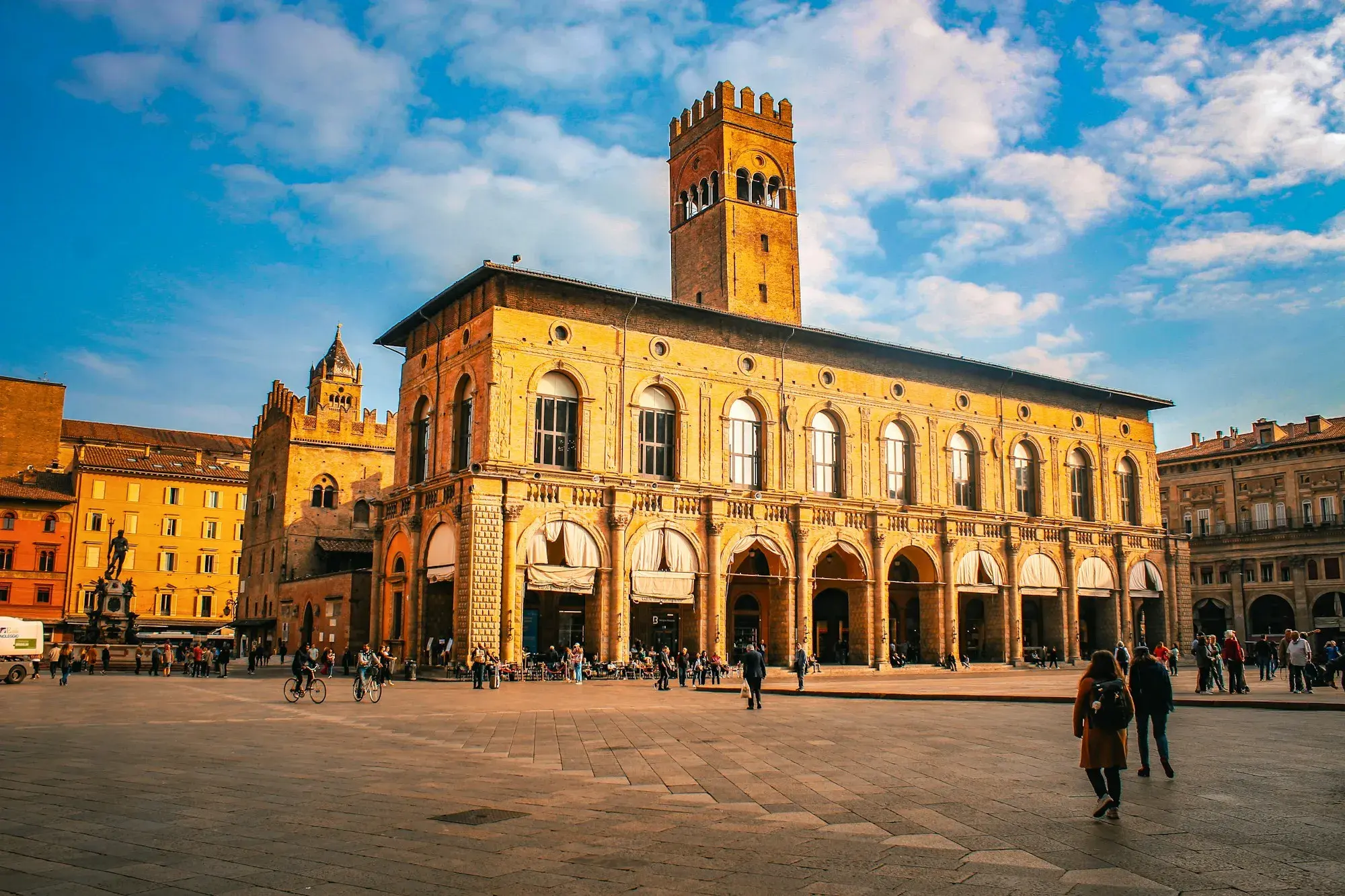 Palazzo del Podestà on Piazza Maggiore in Bologna, a long arcaded building with a brick clock tower, under a blue sky