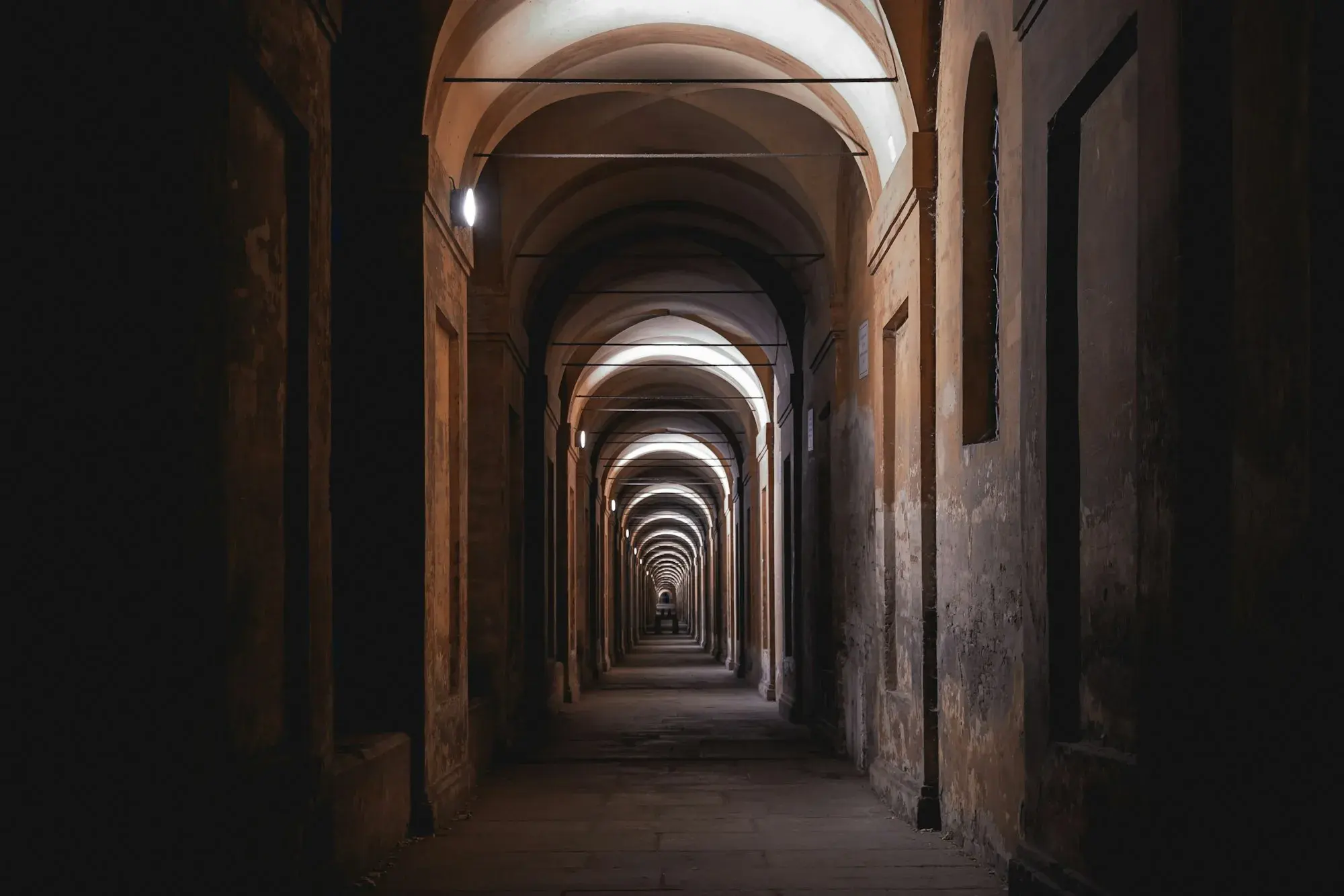 Looking along the long, narrow portico of San Luca in Bologna, a repeating row of arches in shadow