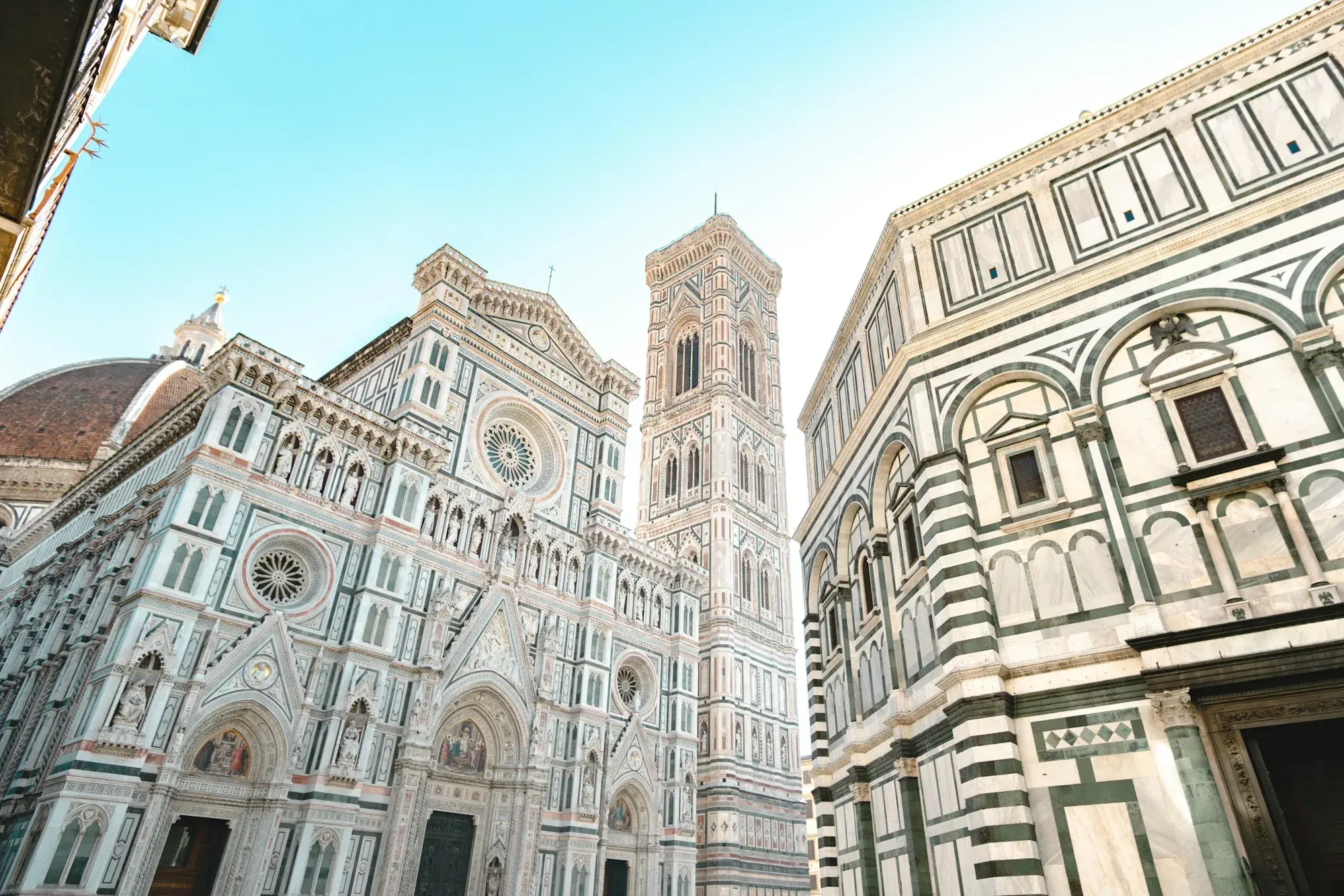 The marble façade of Florence Cathedral with Giotto's bell tower rising beside it under a blue sky