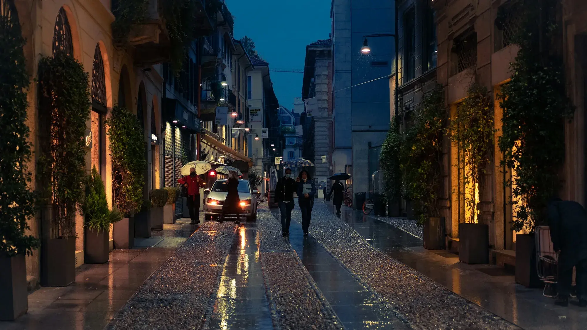 A street in the Brera district of Milan at night, with people walking past lit shopfronts