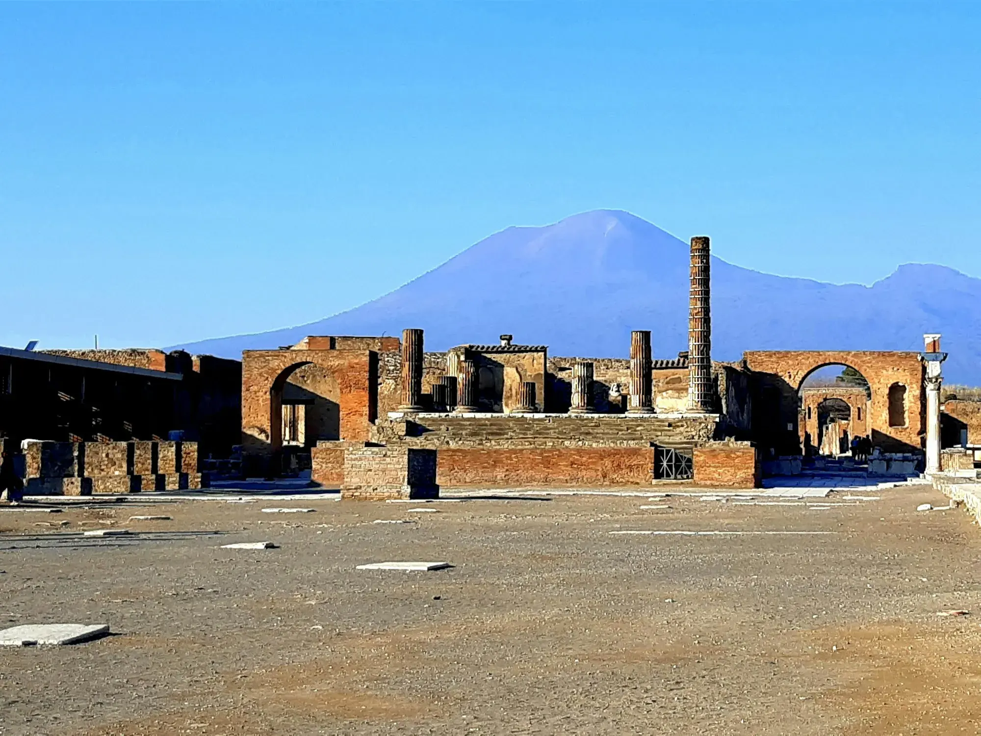 The ruins of the Forum at Pompeii with Mount Vesuvius rising behind under a blue sky