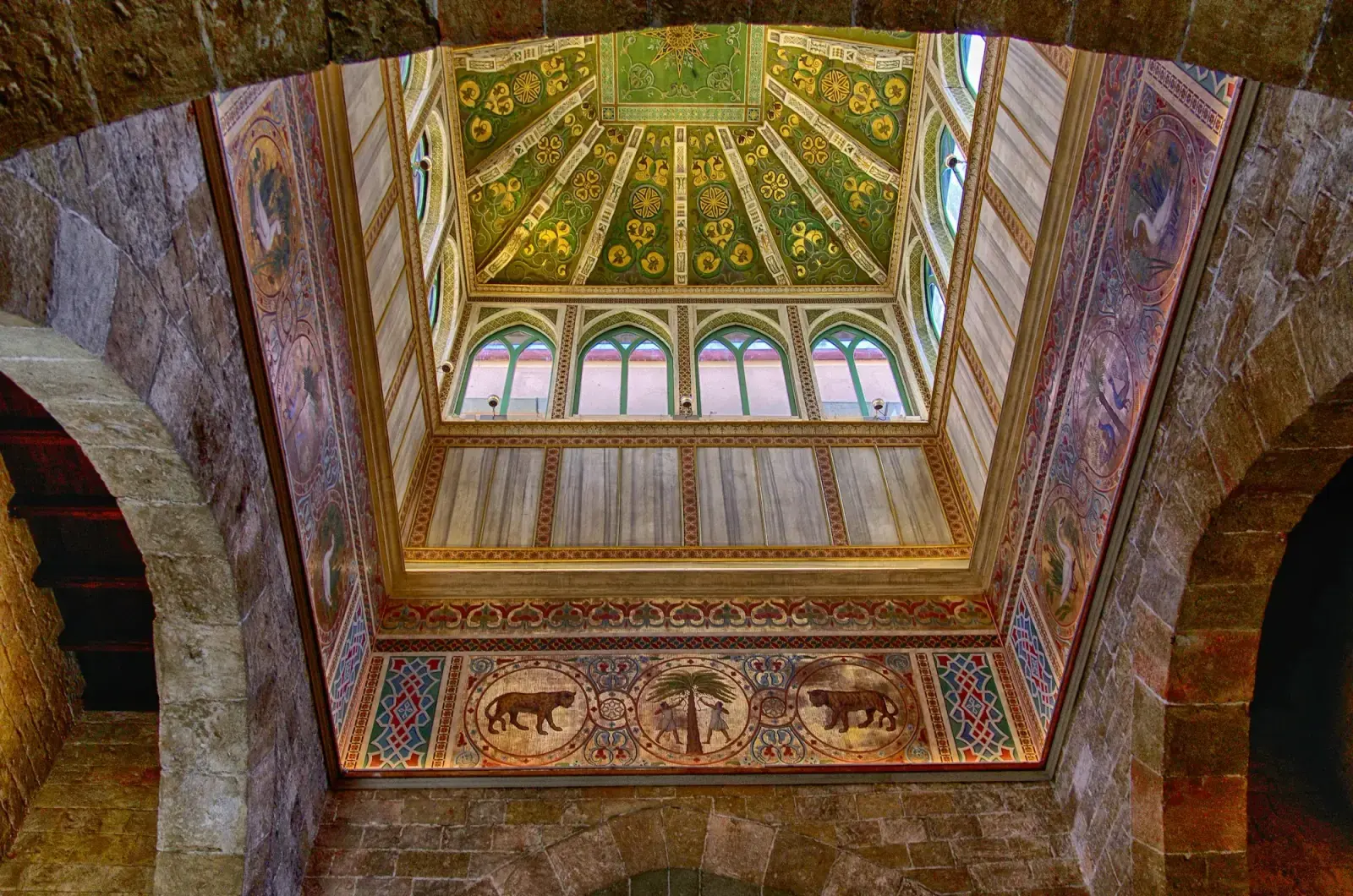 A room in the Palazzo dei Normanni with walls and vault covered in mosaics of animals and palm trees on a gold ground, under a skylight