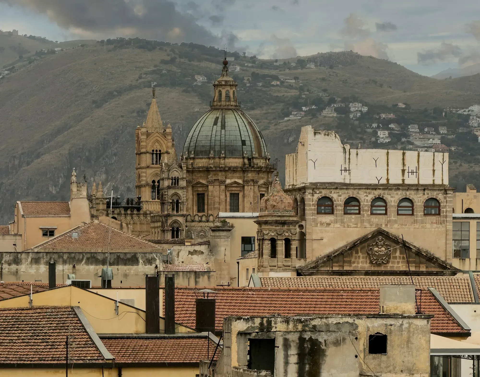 The dome and Gothic towers of Palermo Cathedral rising above the city's rooftops, with mountains behind