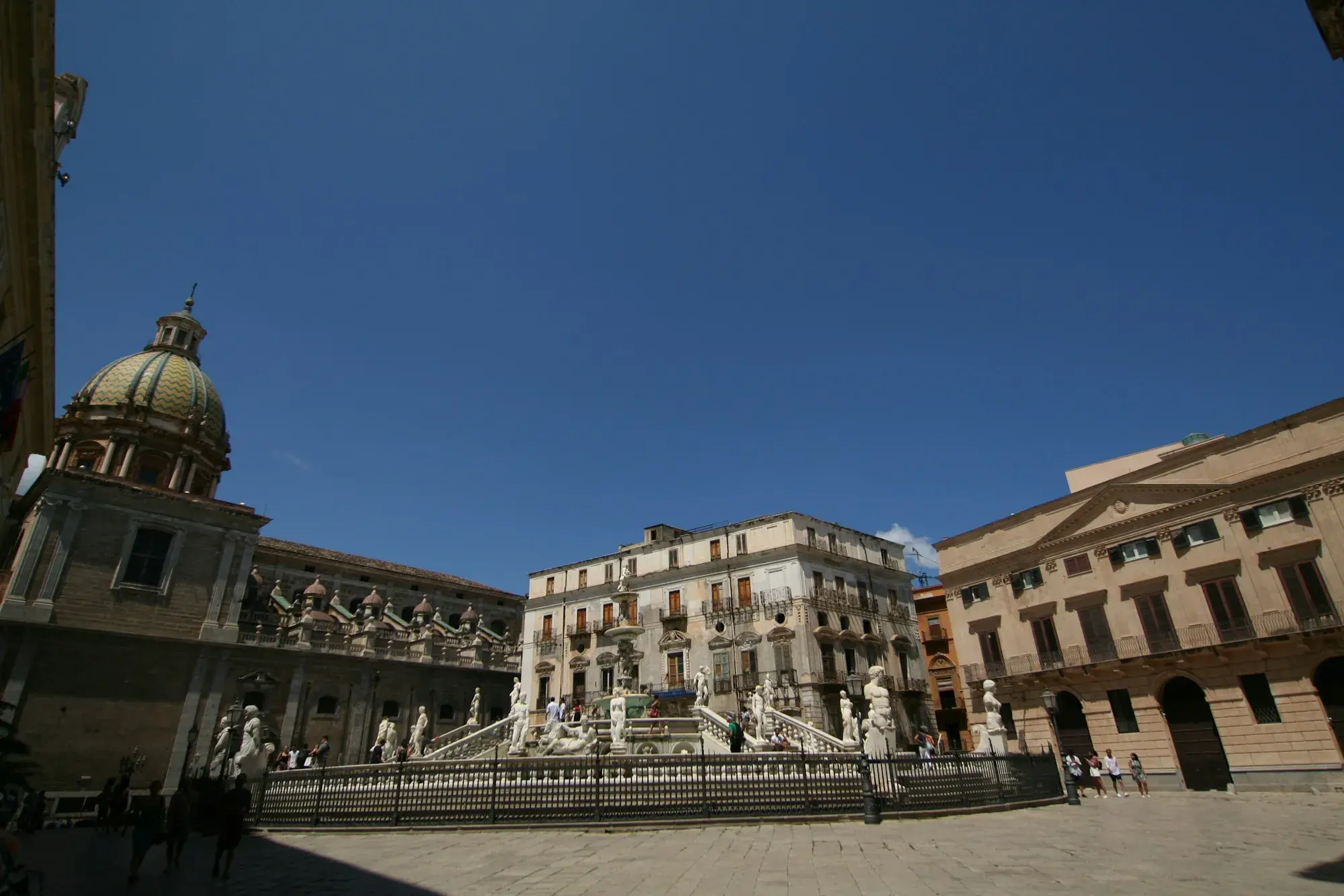 Piazza Pretoria in Palermo with its large marble fountain and statues, surrounded by palaces, with a church dome on the left
