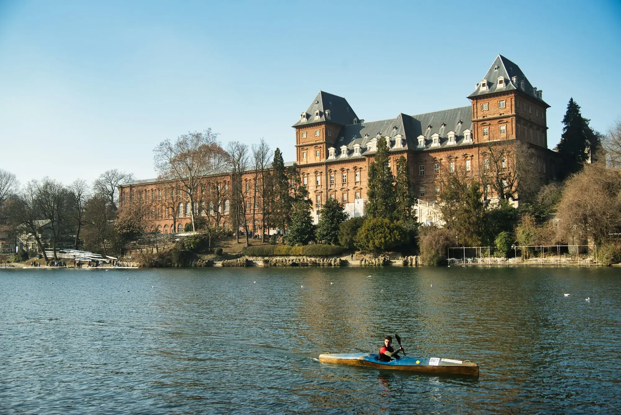 The Valentino Castle seen across the River Po in Turin, with a kayaker on the water in front
