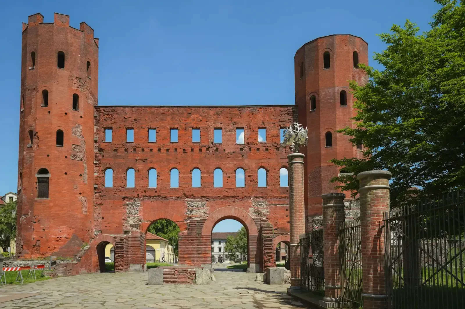 The Porta Palatina in Turin, a Roman brick gateway with two tall polygonal towers, beside green trees