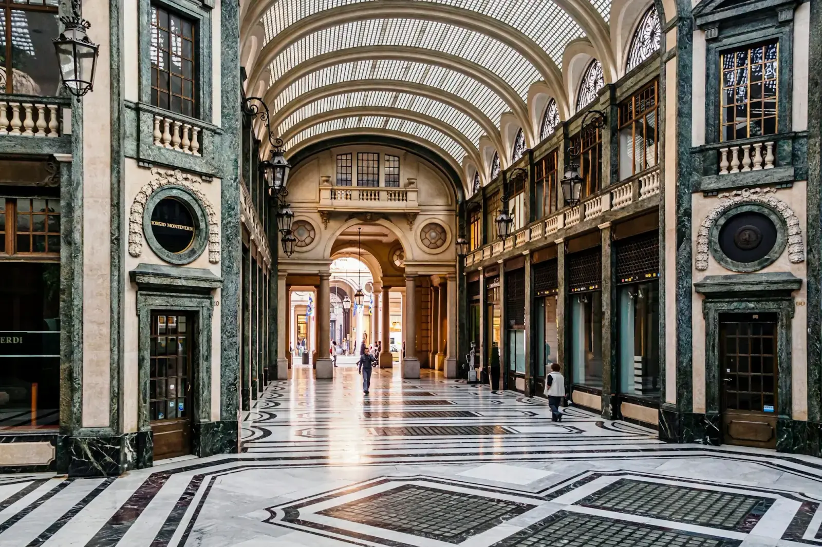 A glass-roofed shopping arcade in central Turin with marble floors, ornate shopfronts and lamps
