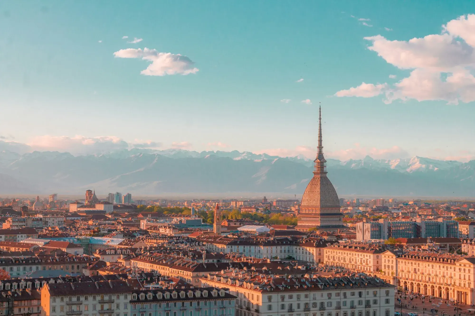 Turin's rooftops at sunset with the tall spire of the Mole Antonelliana and the snow-capped Alps on the horizon