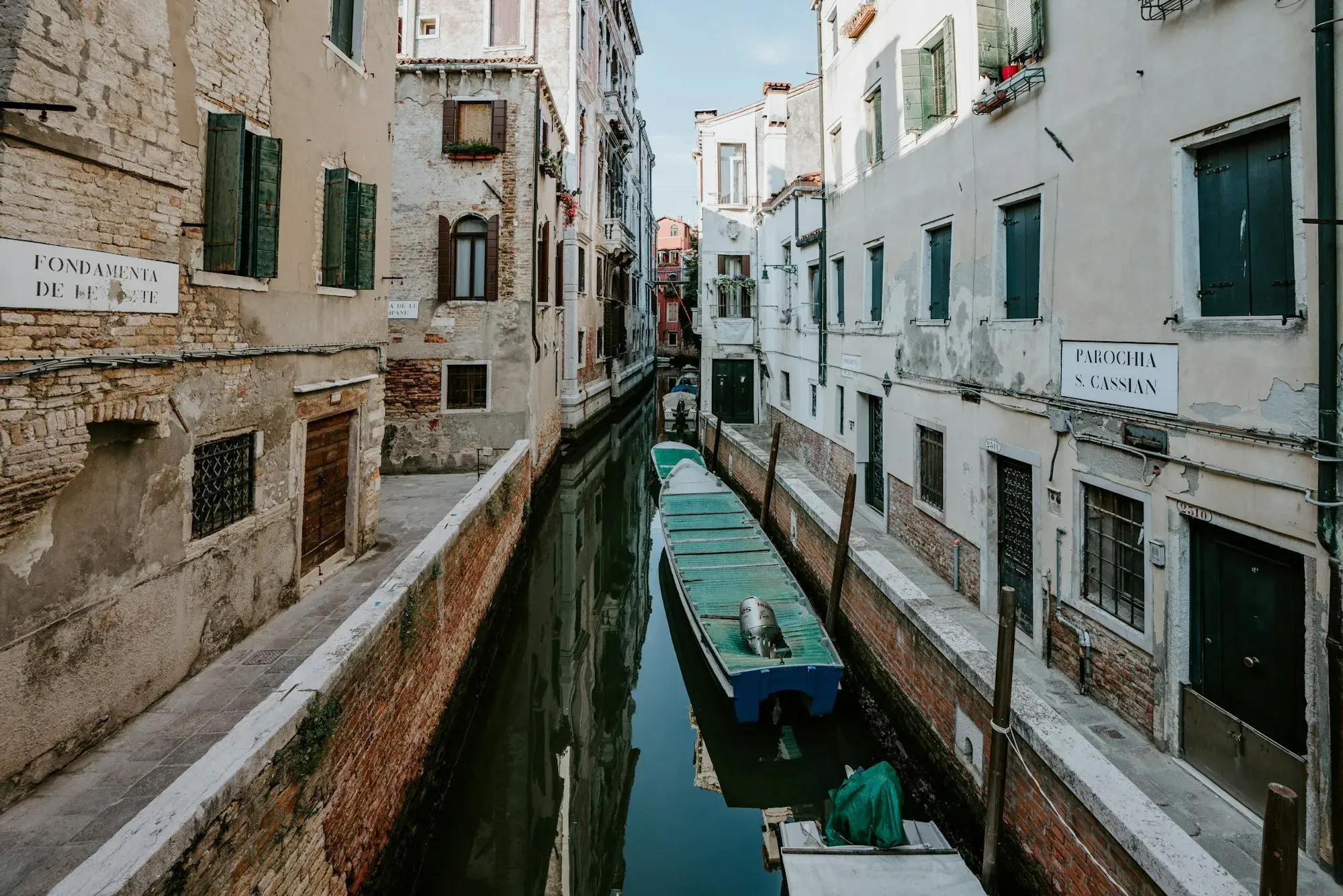 A narrow, quiet residential canal in Venice with a small blue boat moored between old buildings
