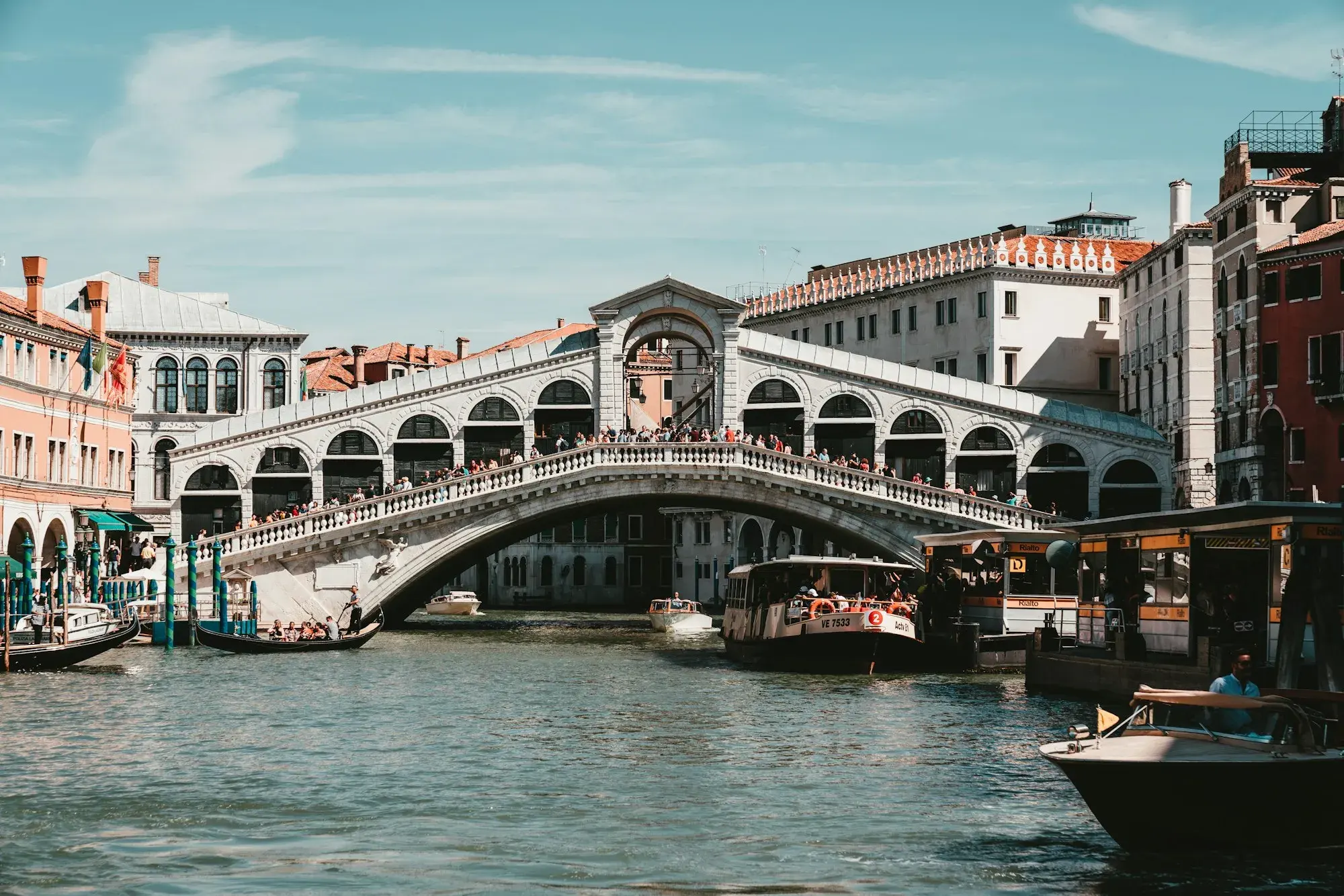 The Rialto Bridge in Venice, a single stone arch over the Grand Canal, with boats and palaces along the water