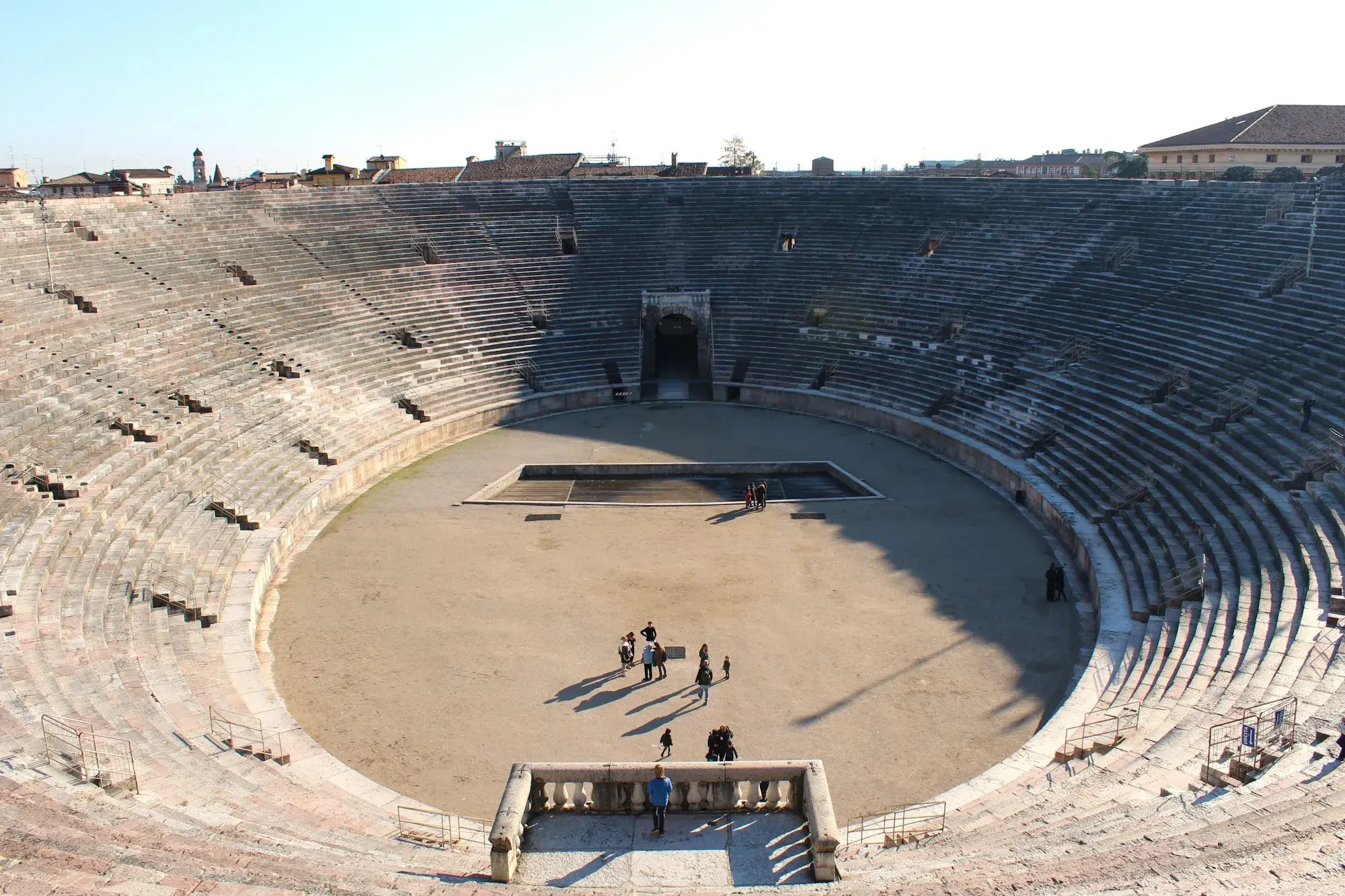 Inside the Roman Arena of Verona, with rows of stone steps rising around the oval floor and a few visitors below