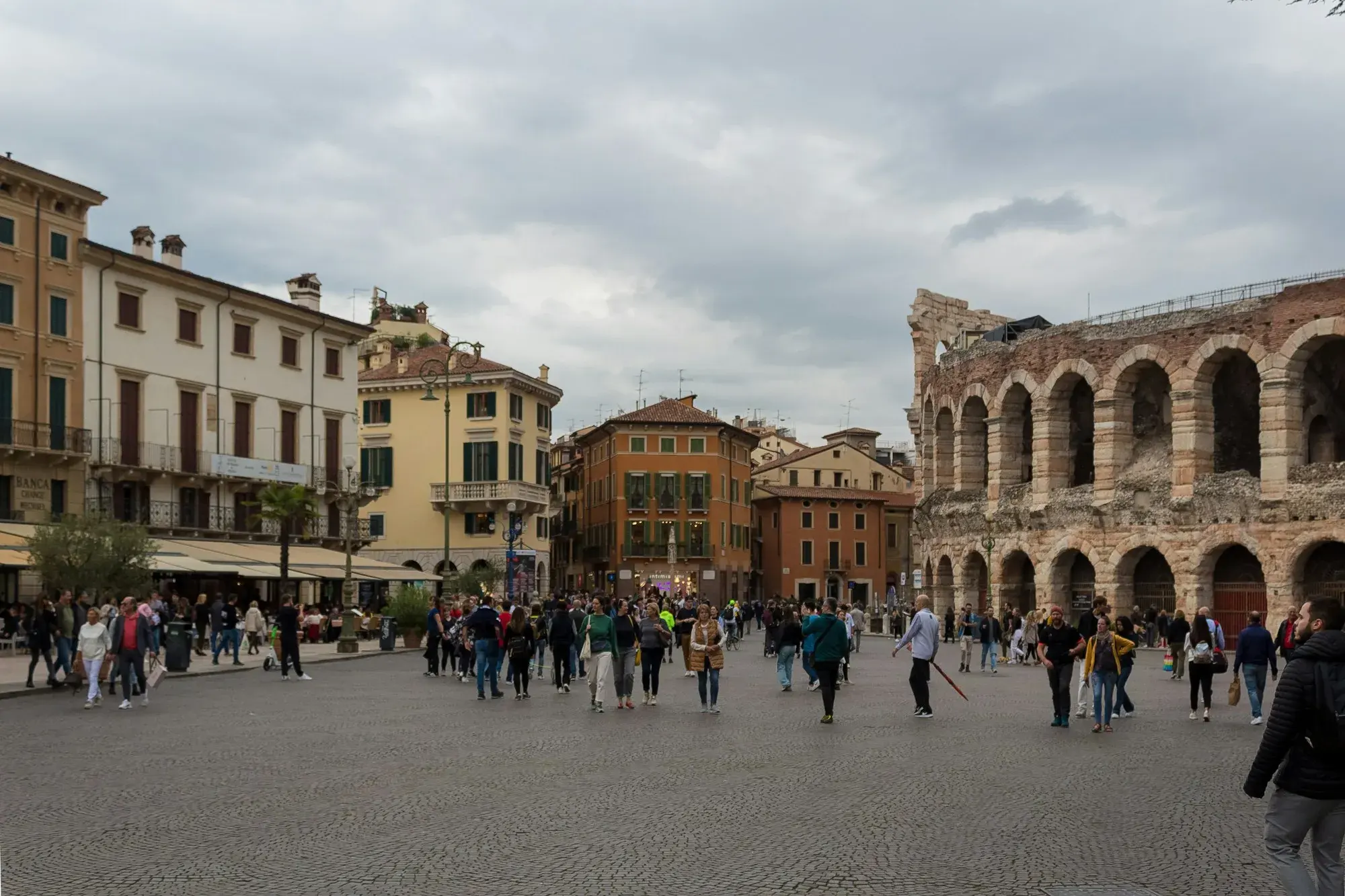 Piazza Bra in Verona with people walking across the square and the Roman Arena's arches on the right