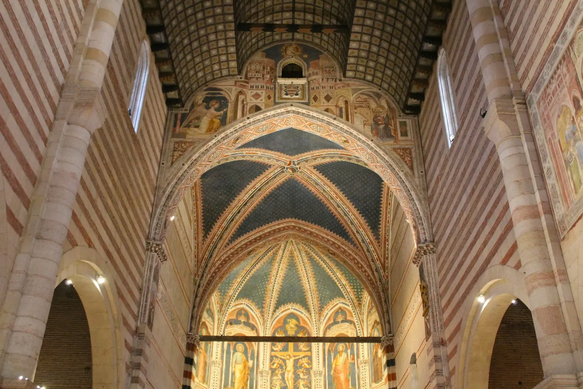 The interior of the Basilica of San Zeno in Verona, with a painted wooden ceiling, striped arches and frescoes above the raised altar