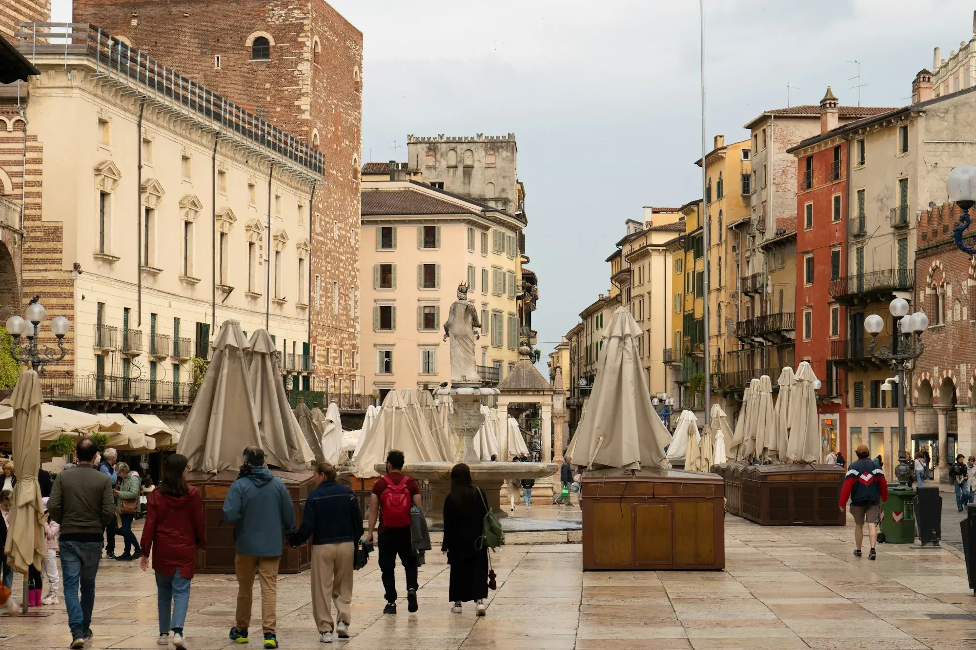 Piazza delle Erbe in Verona with closed market umbrellas, the Madonna Verona fountain and historic palaces, with people walking