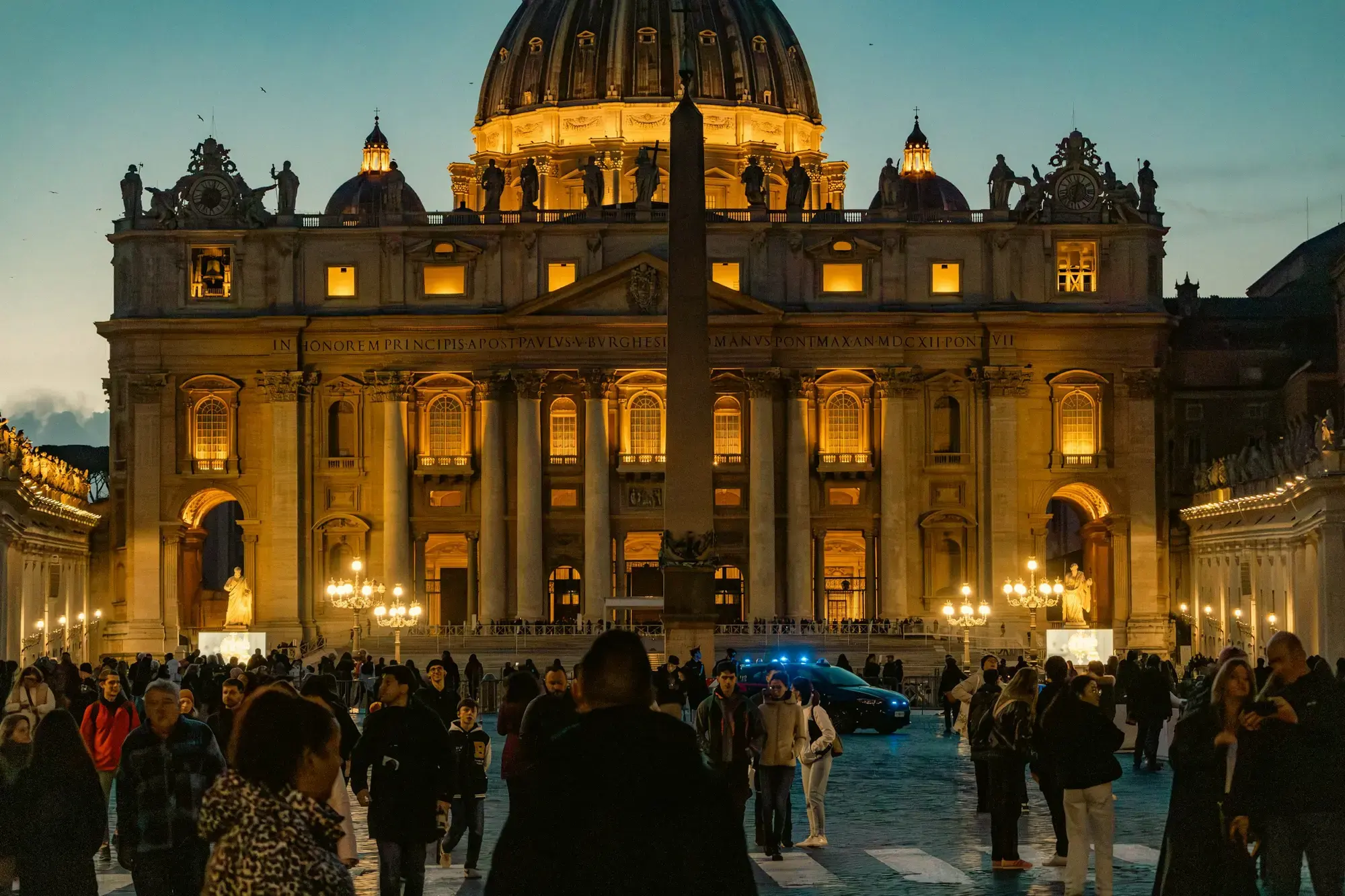 La Basilica di San Pietro illuminata al crepuscolo con visitatori radunati nella piazza antistante