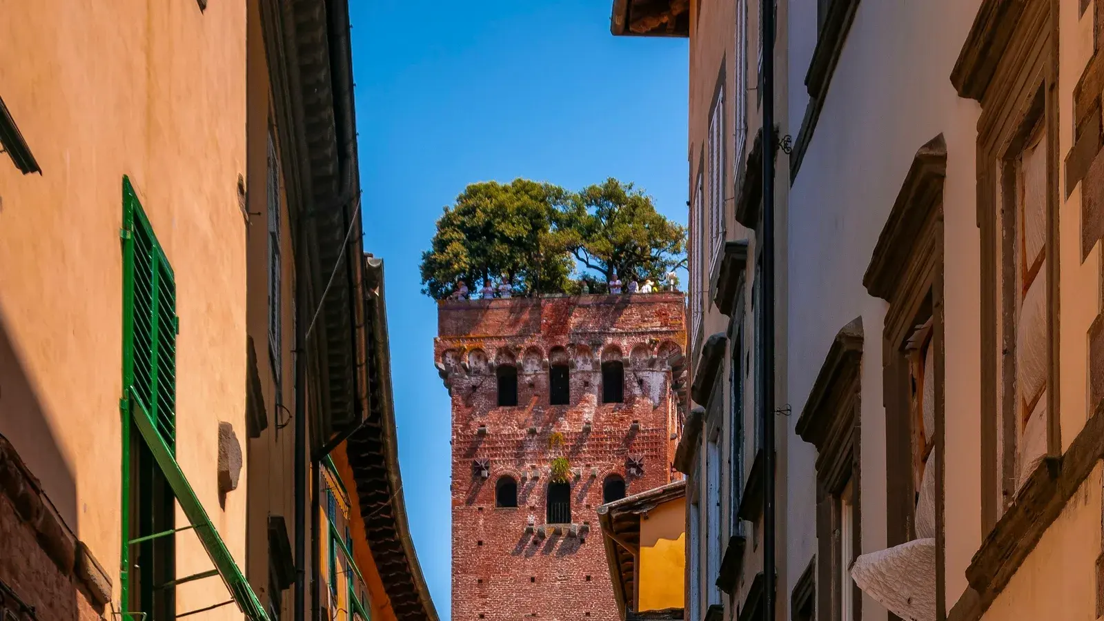 A narrow medieval street in Lucca leading towards one of the city's distinctive brick towers