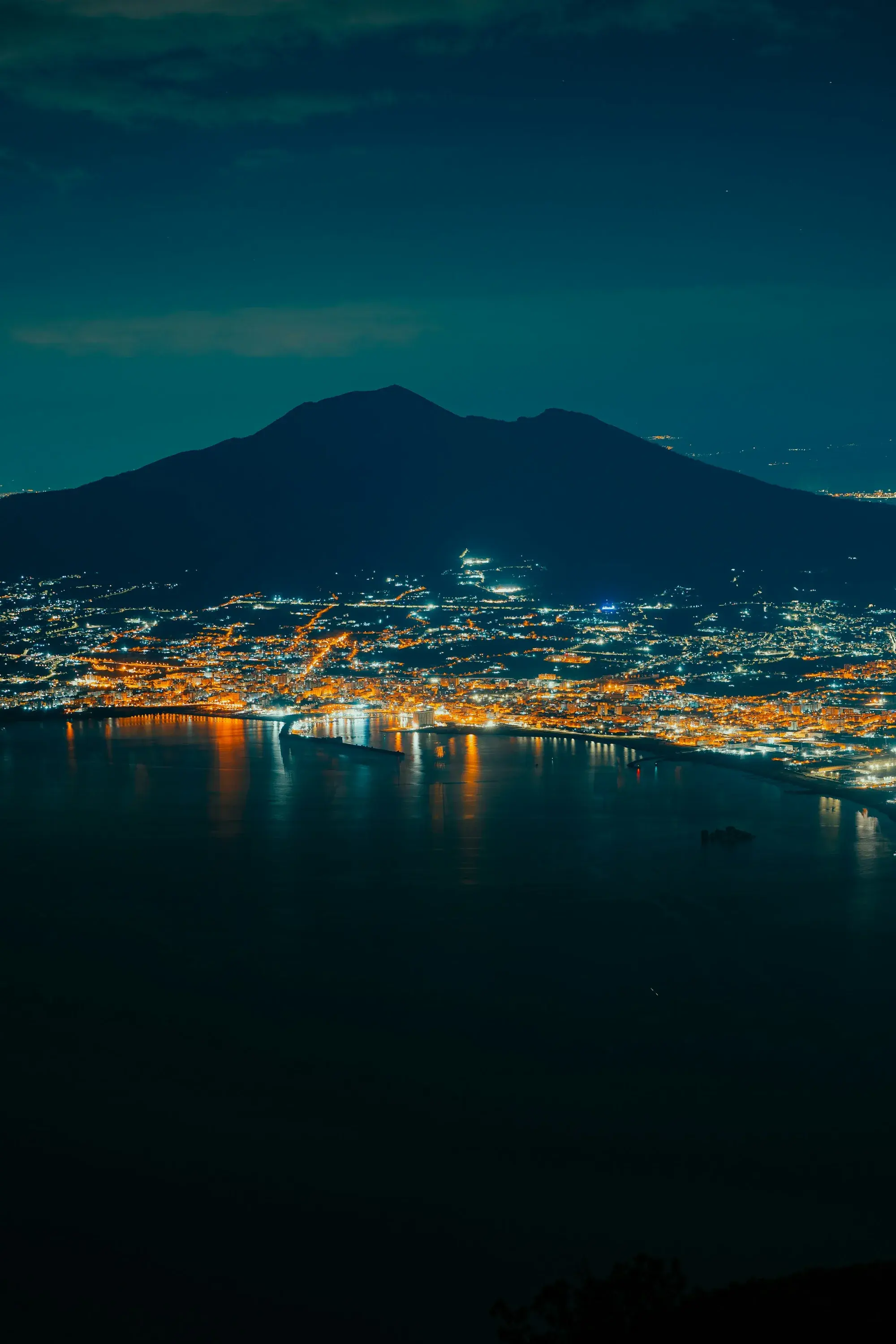 Le luci di Napoli riflesse nel golfo di notte, con la città che sale sul versante collinare alle spalle del lungomare