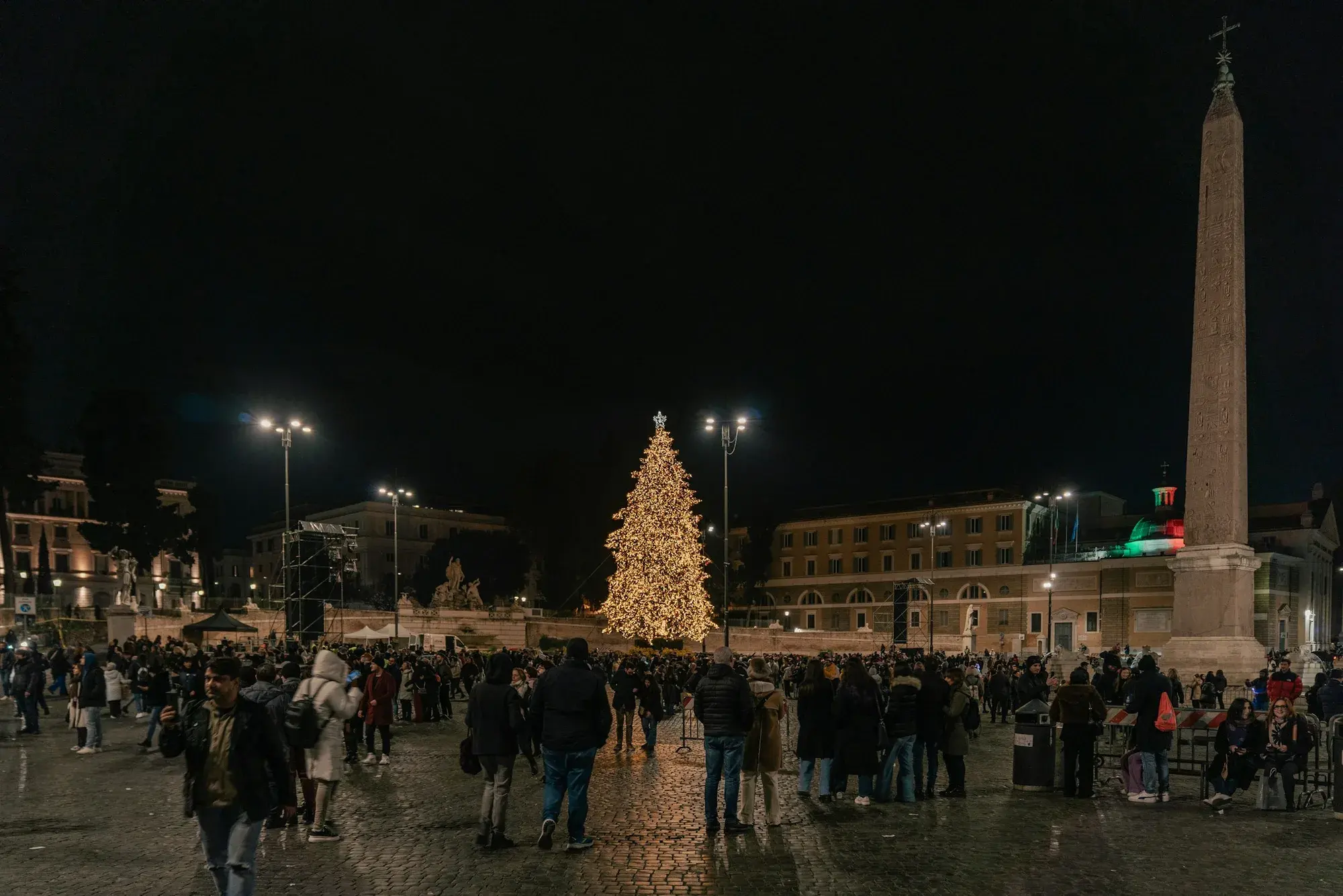 Una folla riunita intorno all'albero di Natale illuminato in Piazza del Popolo a Roma, in una sera d'inverno