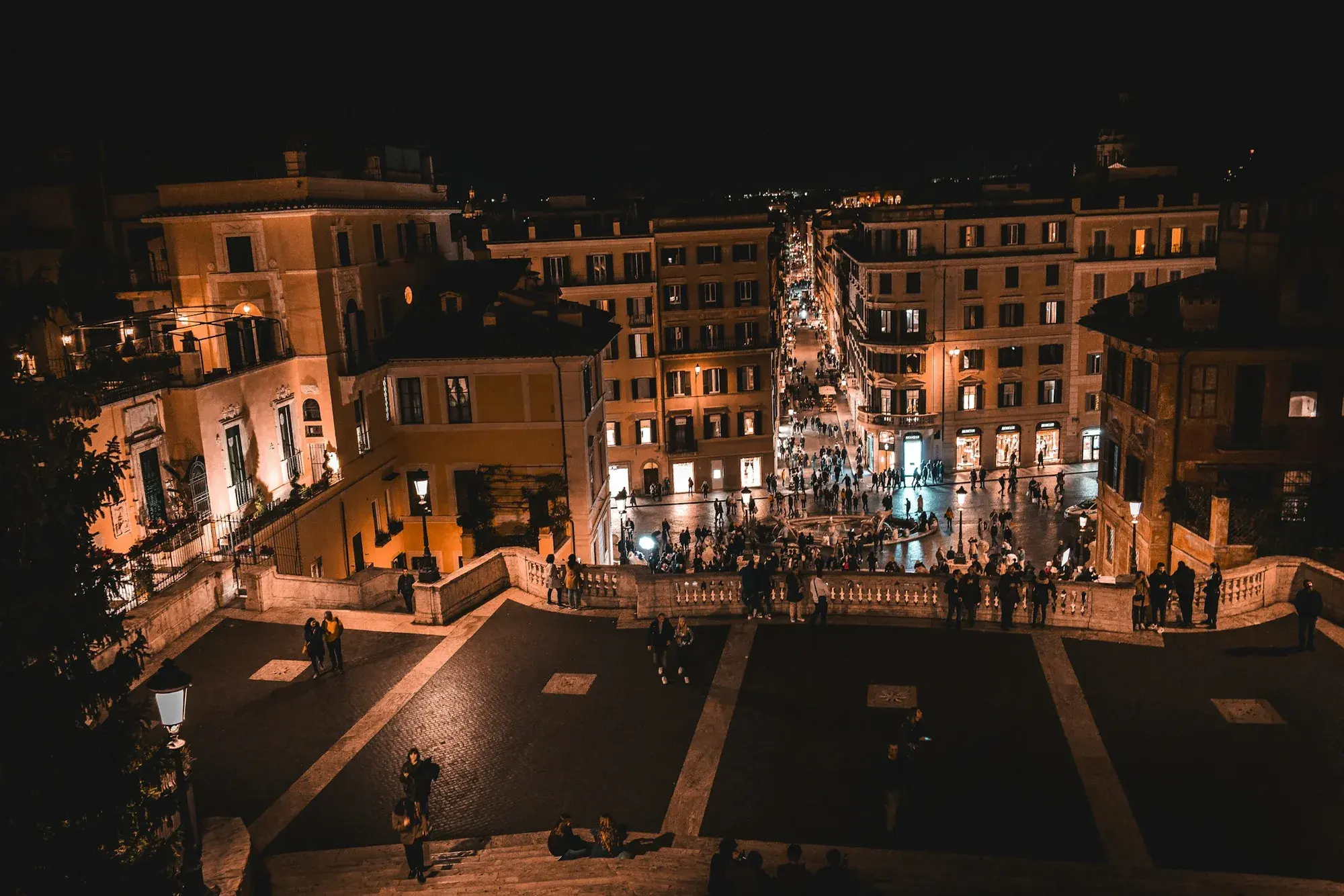 La scalinata di Trinità dei Monti illuminata di notte, con la chiesa in cima e la gente riunita nella piazza sottostante