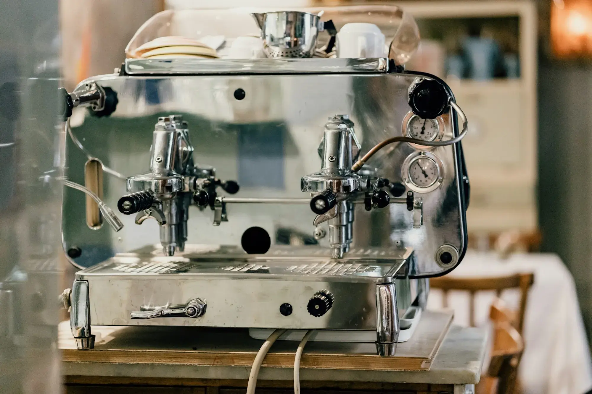 A polished chrome two-group espresso machine with levers and pressure gauges on a counter in a Roman trattoria