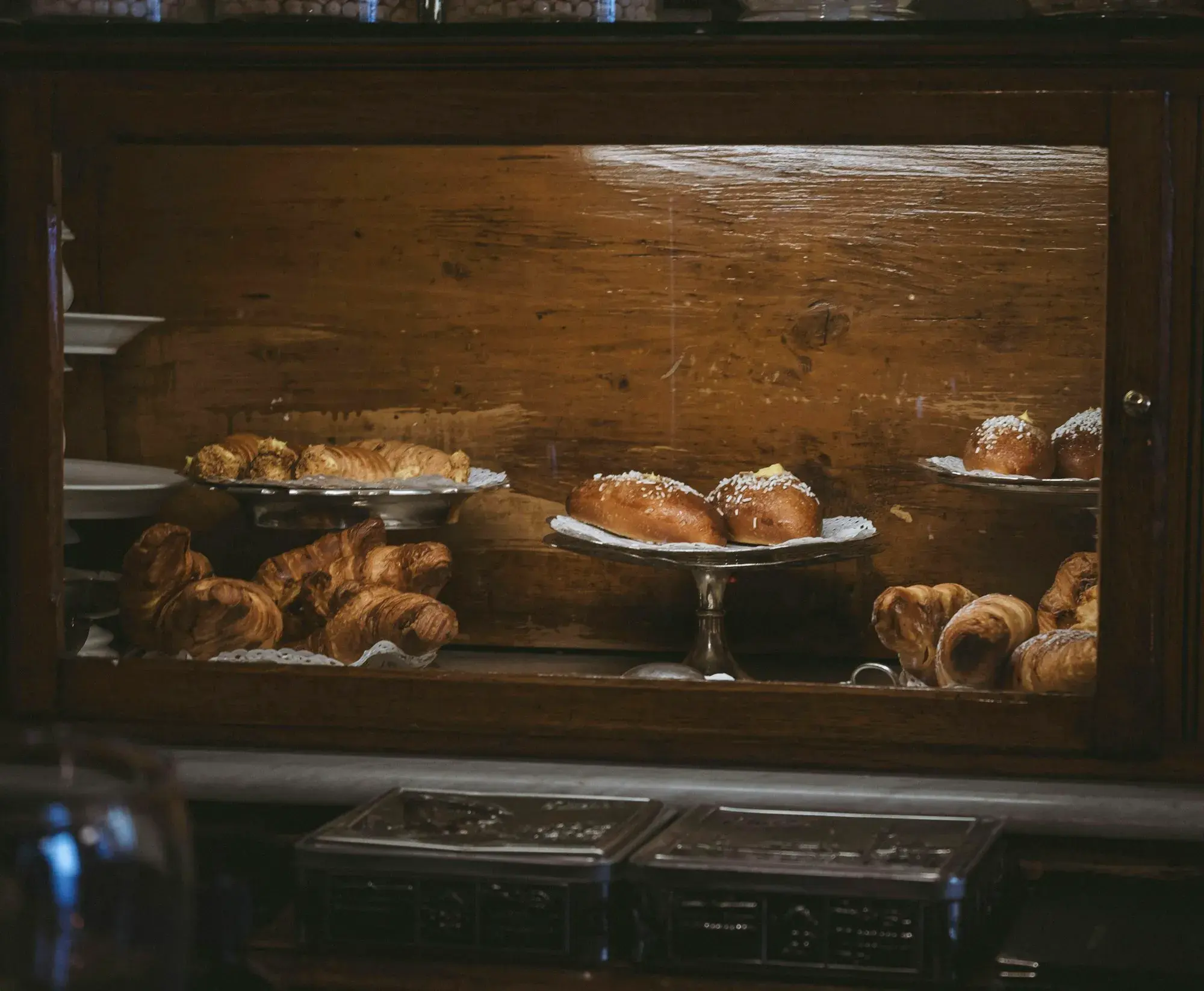 A wooden display case of cornetti and pastries on glass stands inside the Caffè Al Bicerin in Turin