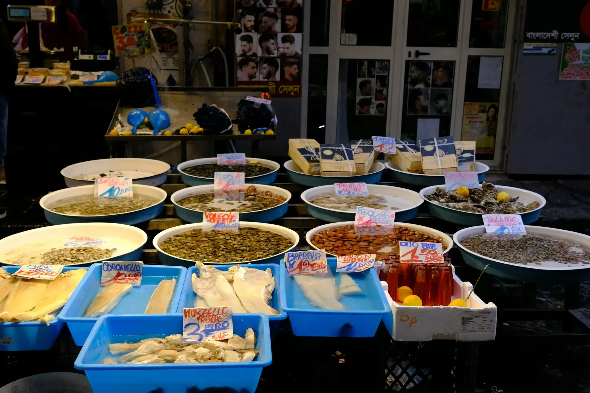 Ciotole di olive di vario tipo e vaschette blu di baccalà con cartellini dei prezzi scritti a mano su un banco di mercato a Napoli