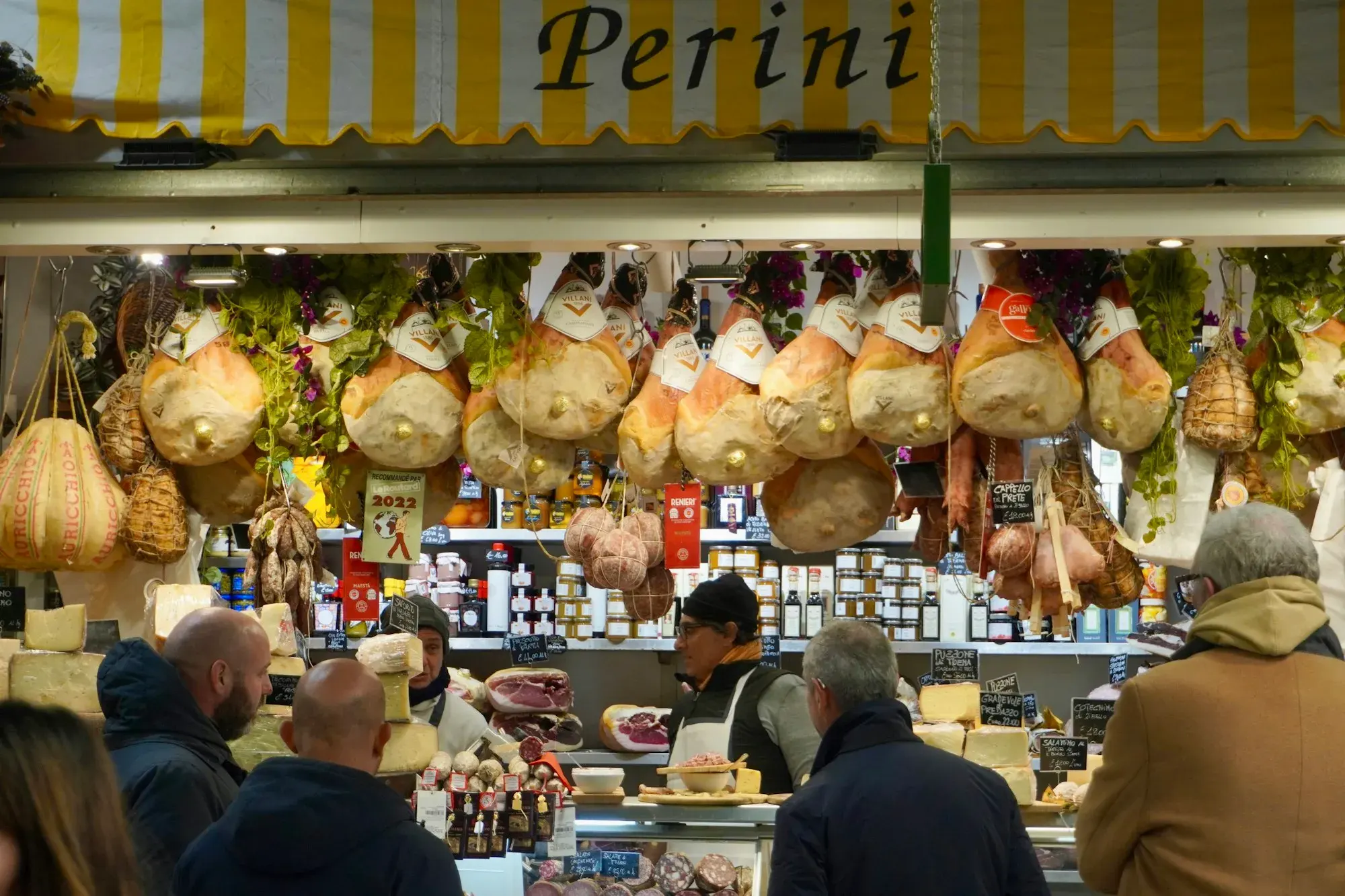 Hams, salami and wheels of cheese hanging above a busy counter at Florence's Mercato Centrale