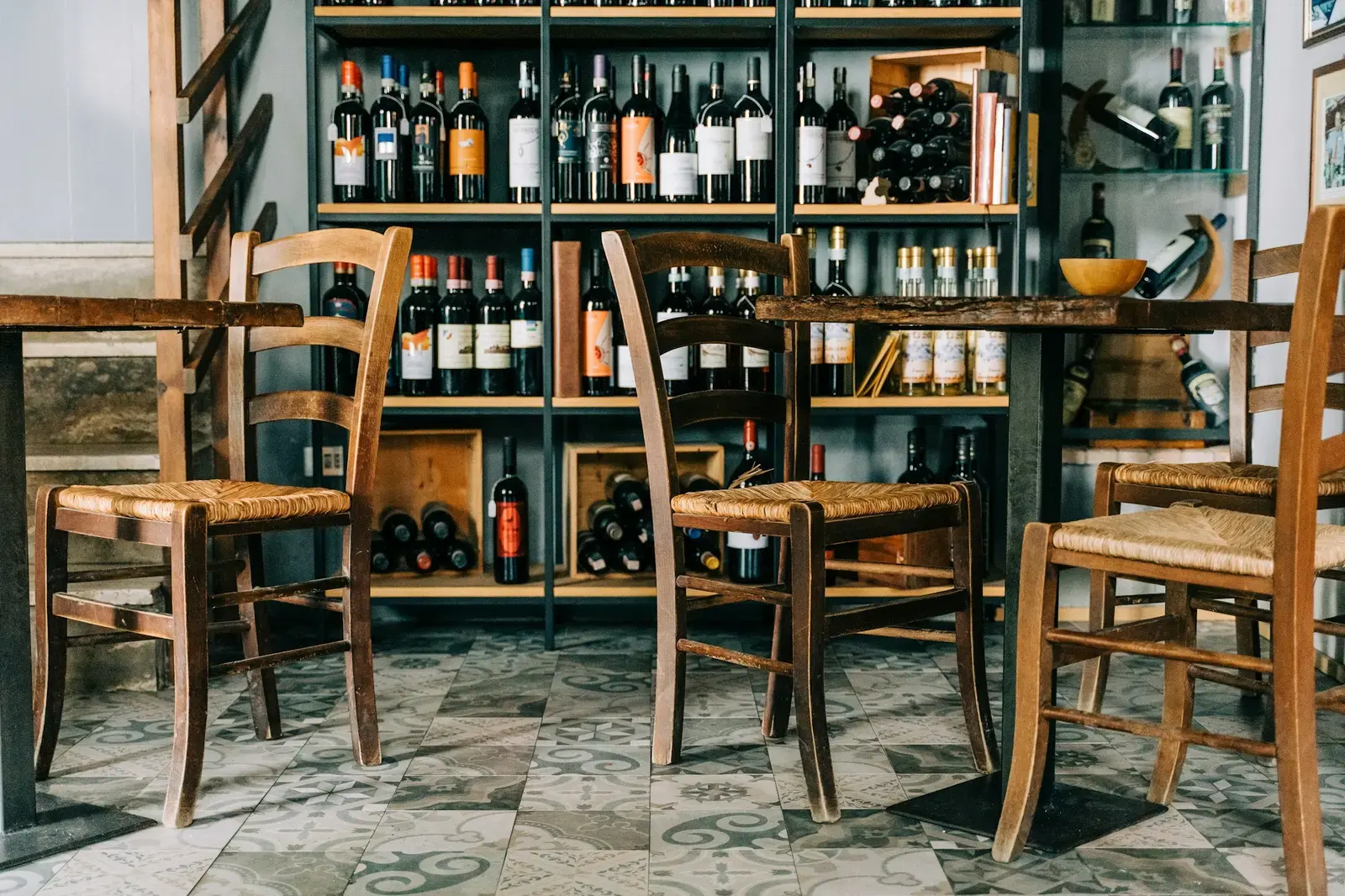 Rush-seated wooden chairs and a small table in front of shelves of wine bottles in a wine shop in Radicofani, Tuscany