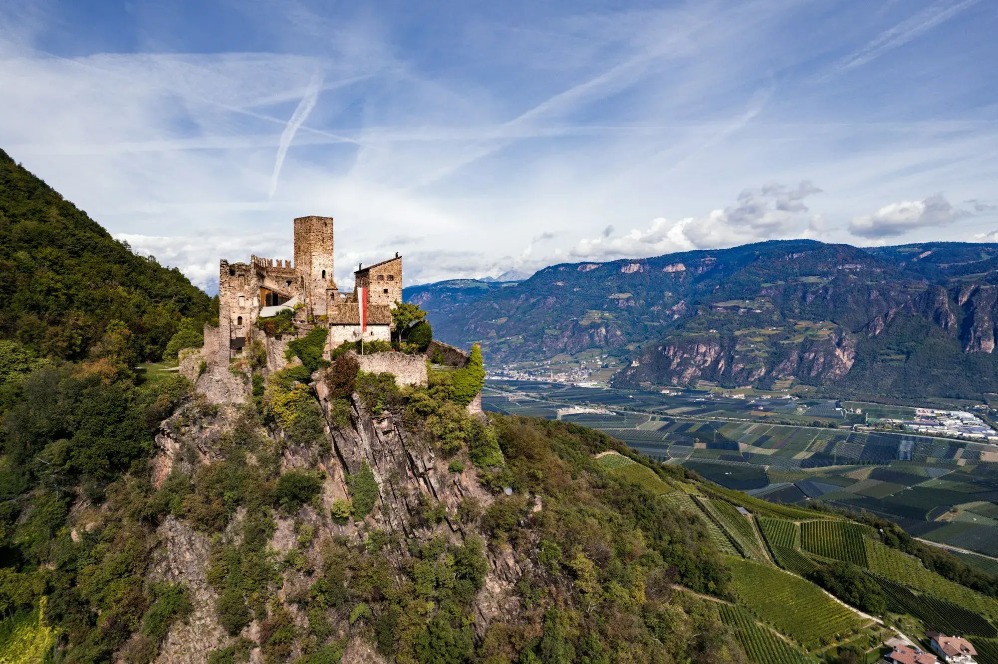 Hocheppan castle on a wooded crag above a wide valley of vineyards and orchards in South Tyrol, with limestone mountains beyond