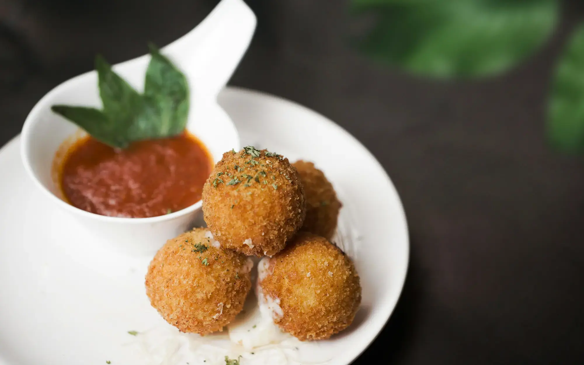 Tre palle di riso fritte e dorate su un piatto bianco, con la panatura croccante