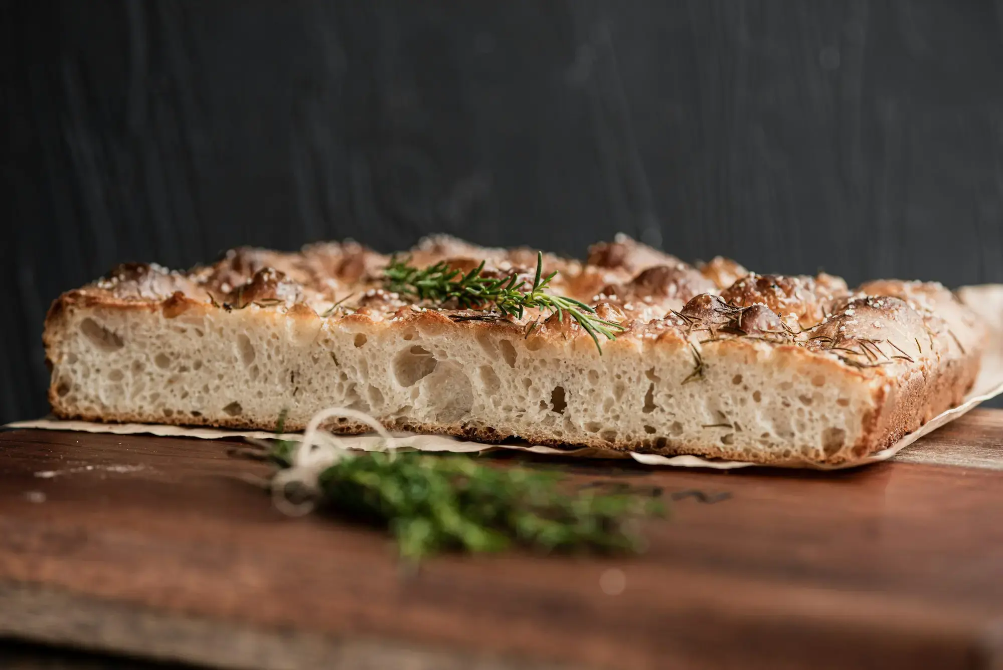 Focaccia appena sfornata con rosmarino e olio d'oliva su un tagliere di legno