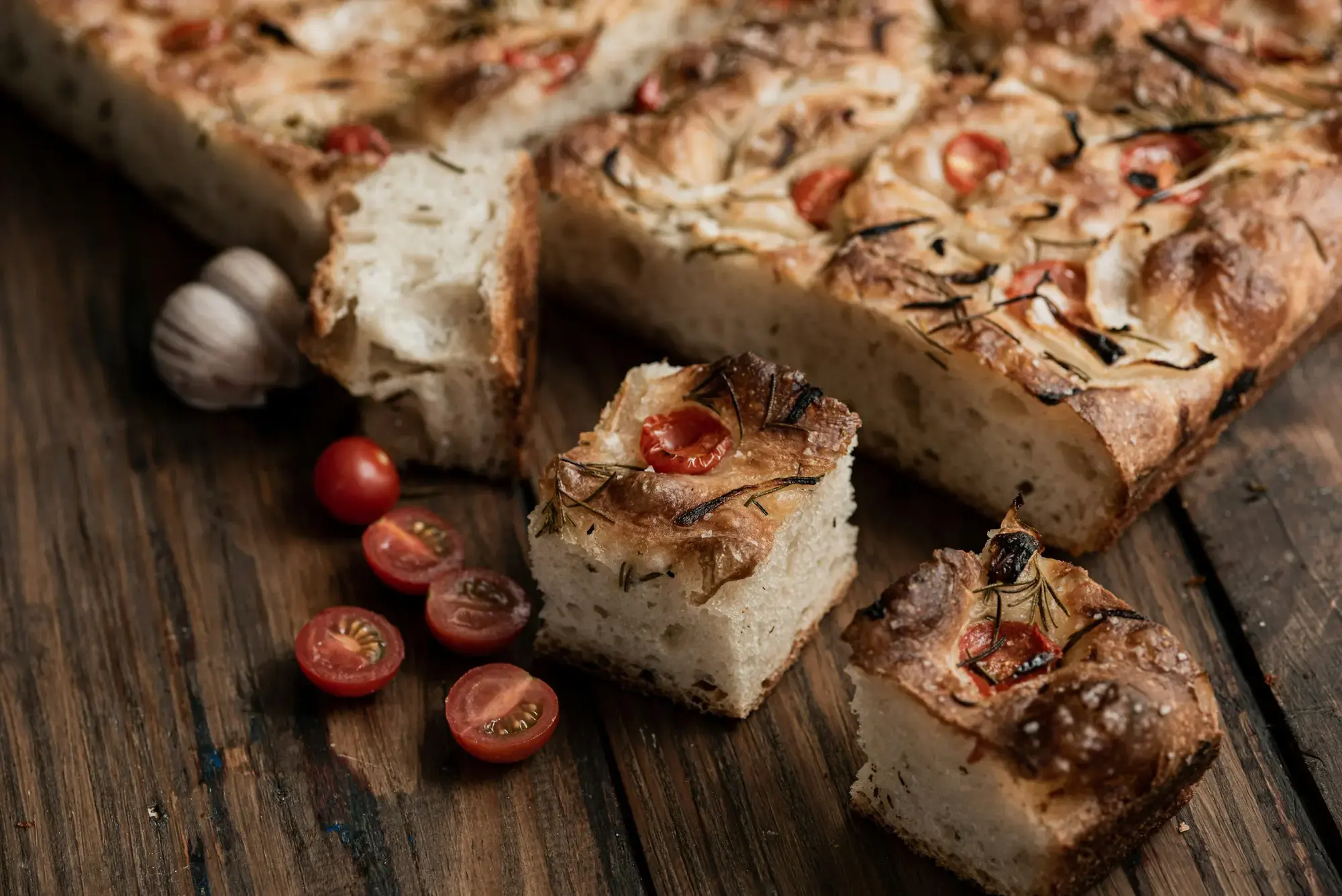 Un pezzo di focaccia con pomodorini ciliegino e aglio su un tagliere di legno