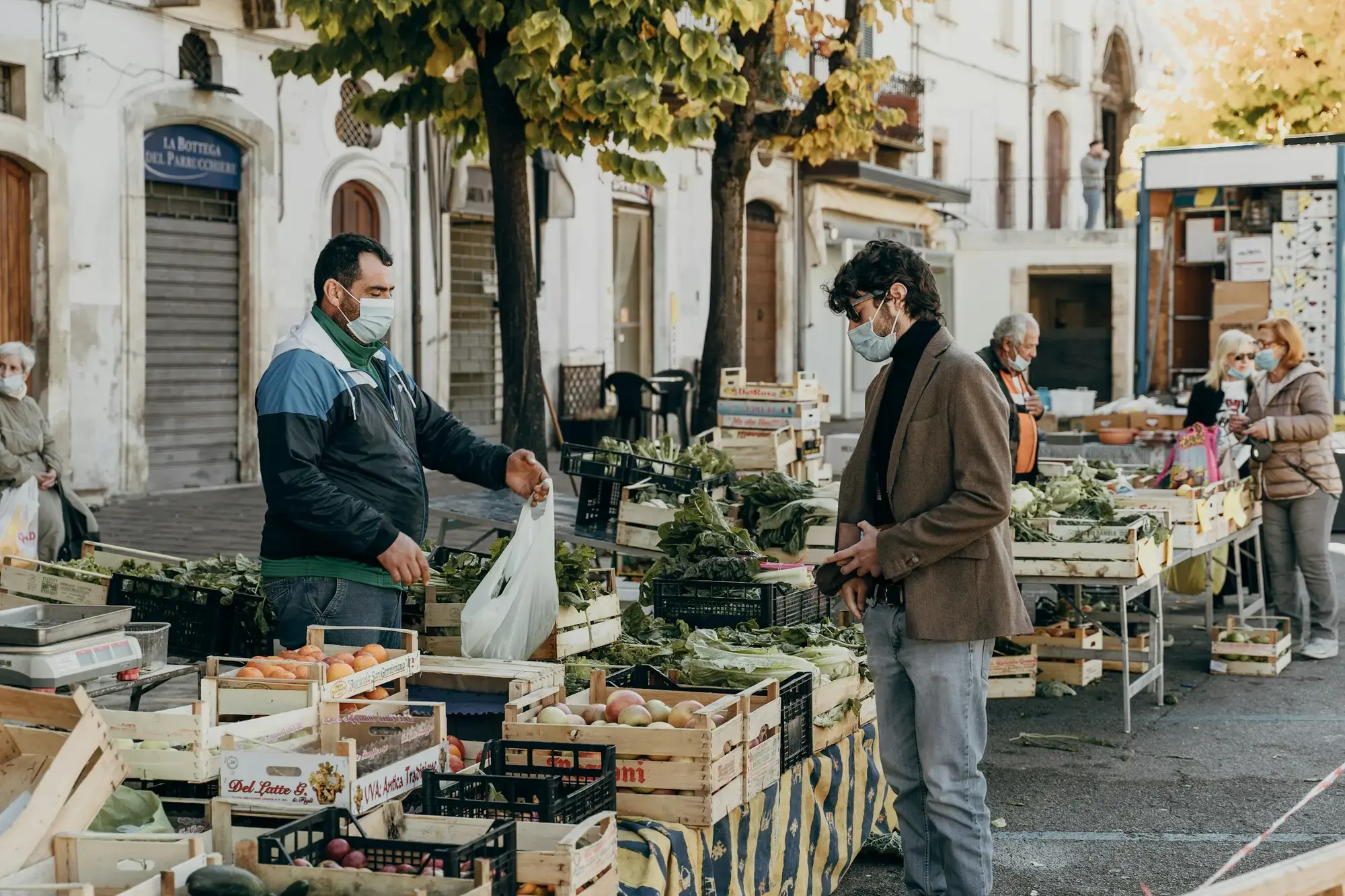 Un venditore con il giaccone verde dietro al banco di un mercato all'aperto