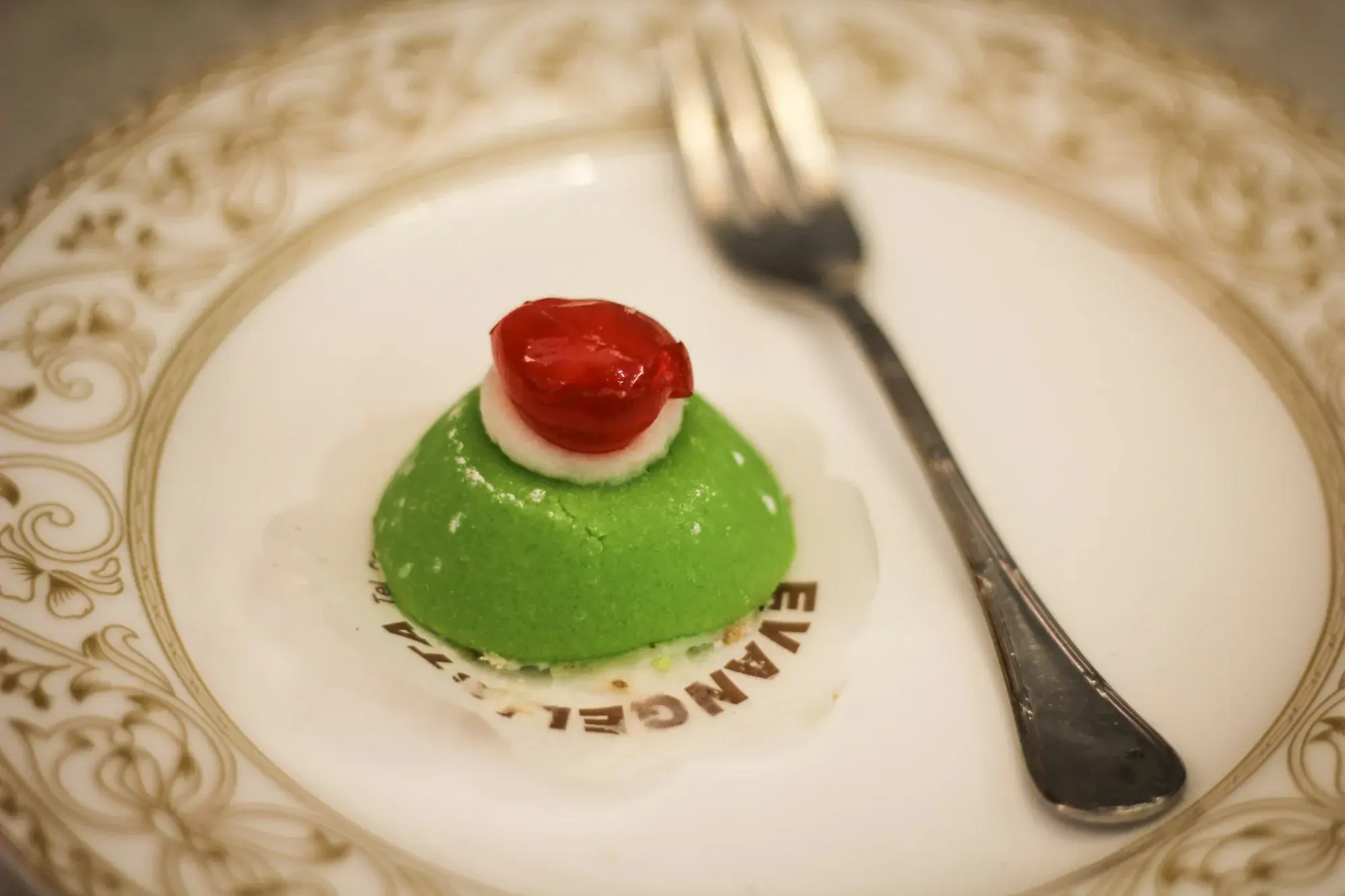 A small individual cassata with green marzipan and a candied cherry on a white plate with a fork