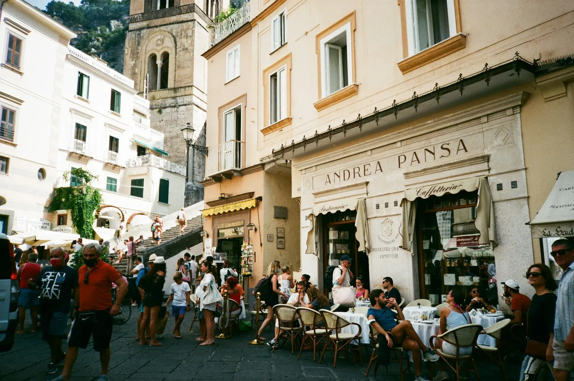 Tables of customers outside a historic pastry shop on the cathedral square in Amalfi, with the bell tower behind