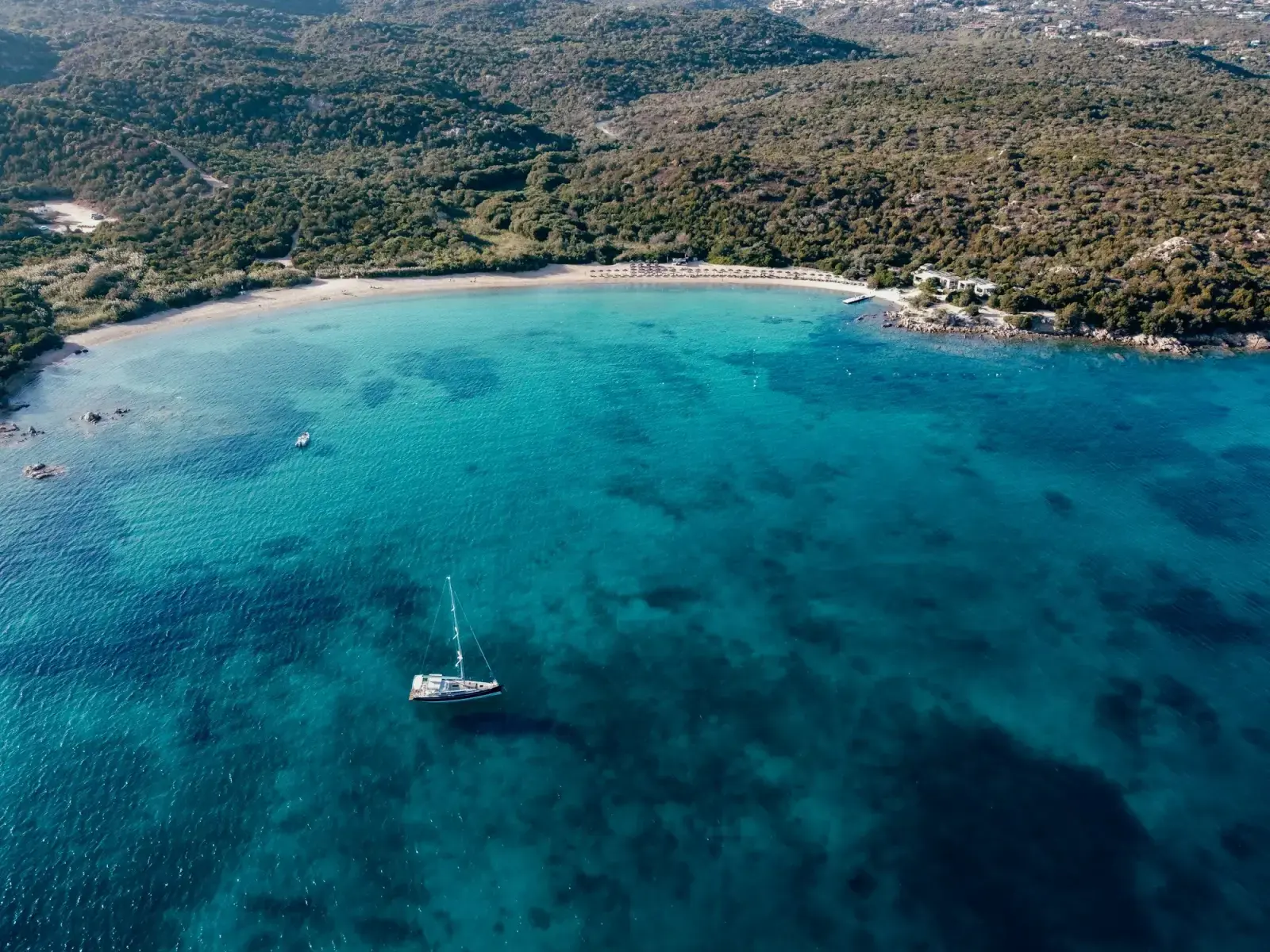Aerial view of a sheltered bay with turquoise water and a moored boat at Cala di Volpe in Sardinia