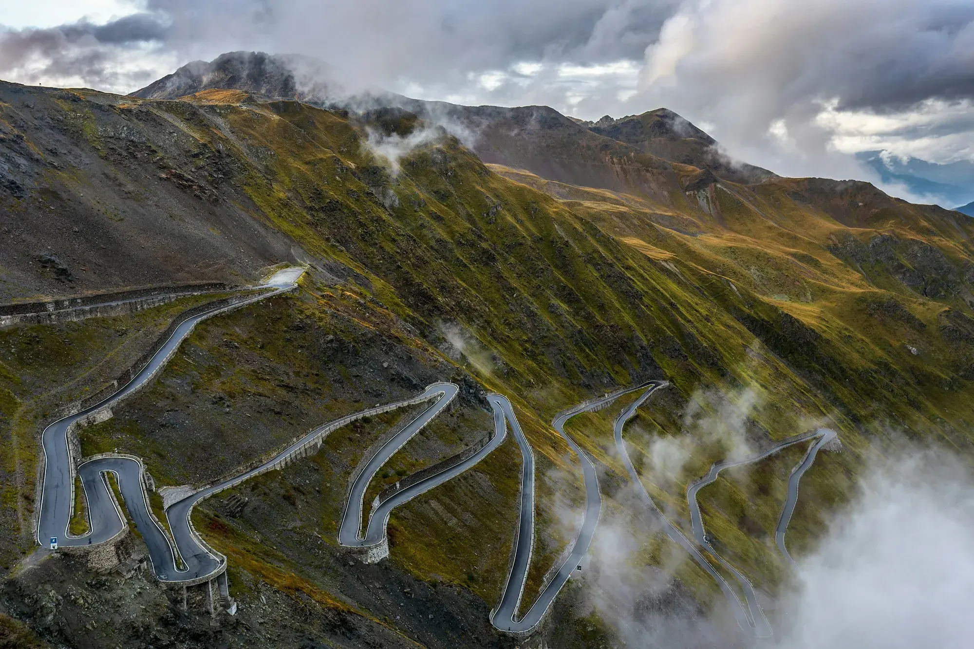 A road climbing through a green mountain valley in a series of hairpin bends in the Italian Alps