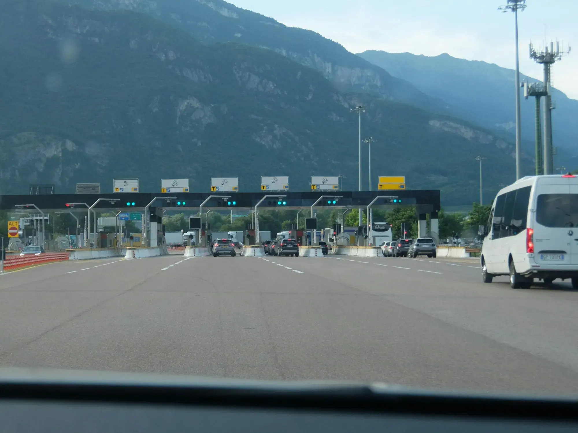 Cars approaching a multi-lane motorway toll plaza near Rovereto with mountains in the background