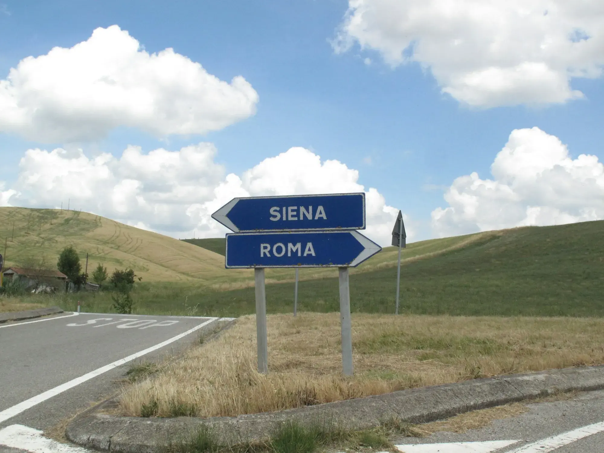 Blue direction signs pointing to Siena and Roma beside a country road in Tuscany