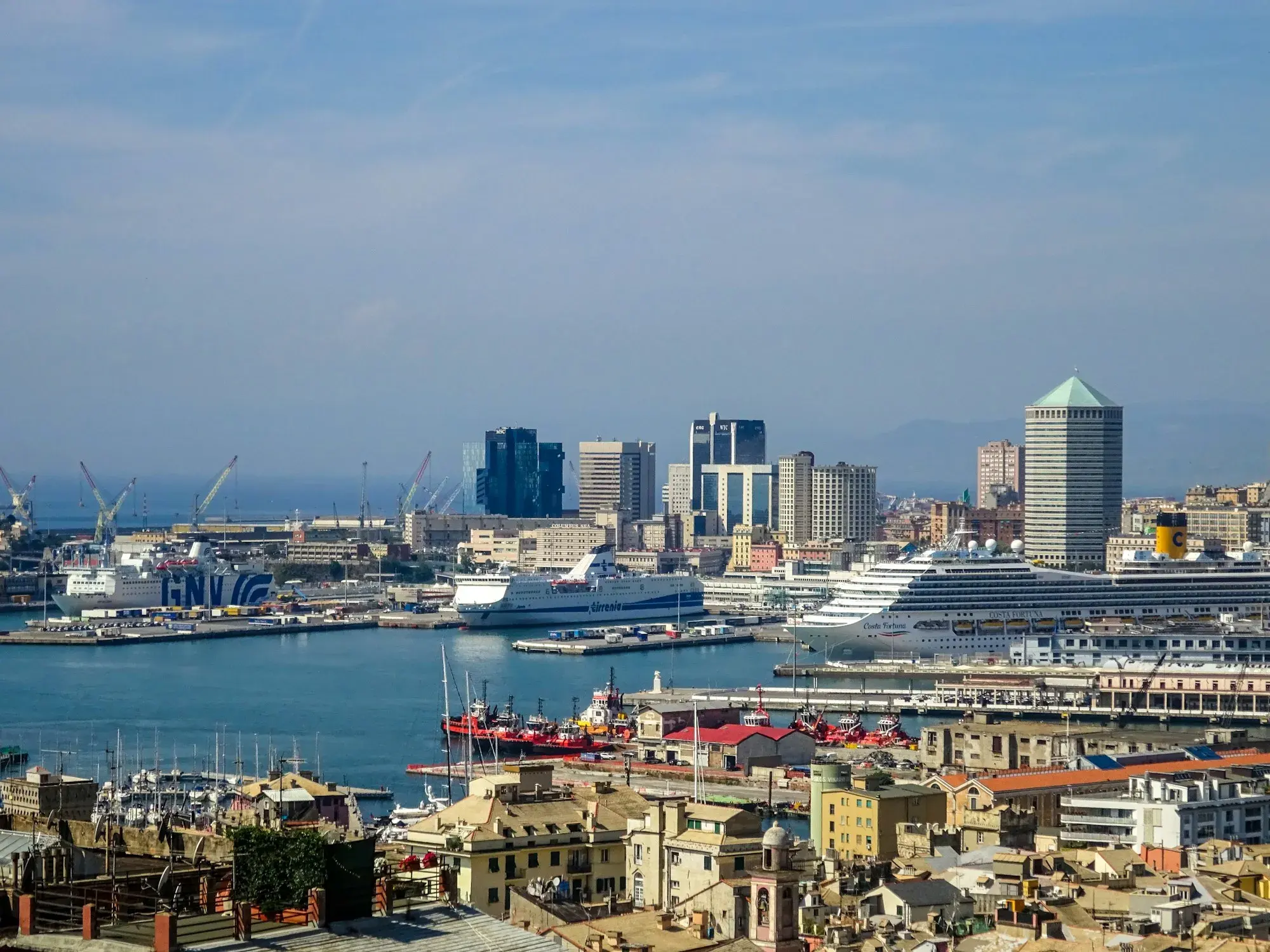 The port of Genoa with ferries and a cruise ship moored in front of the city's towers and hills