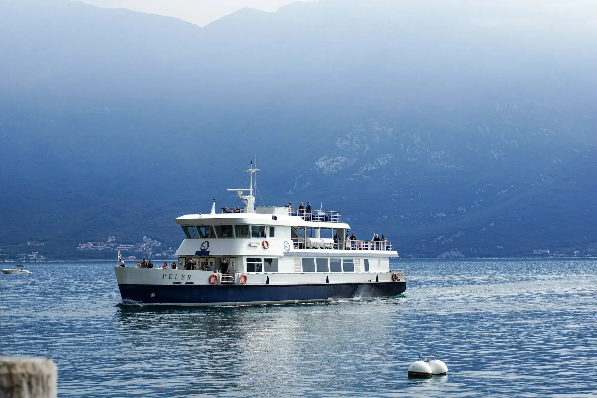 A white passenger boat on Lake Garda near Limone, with misty mountains behind