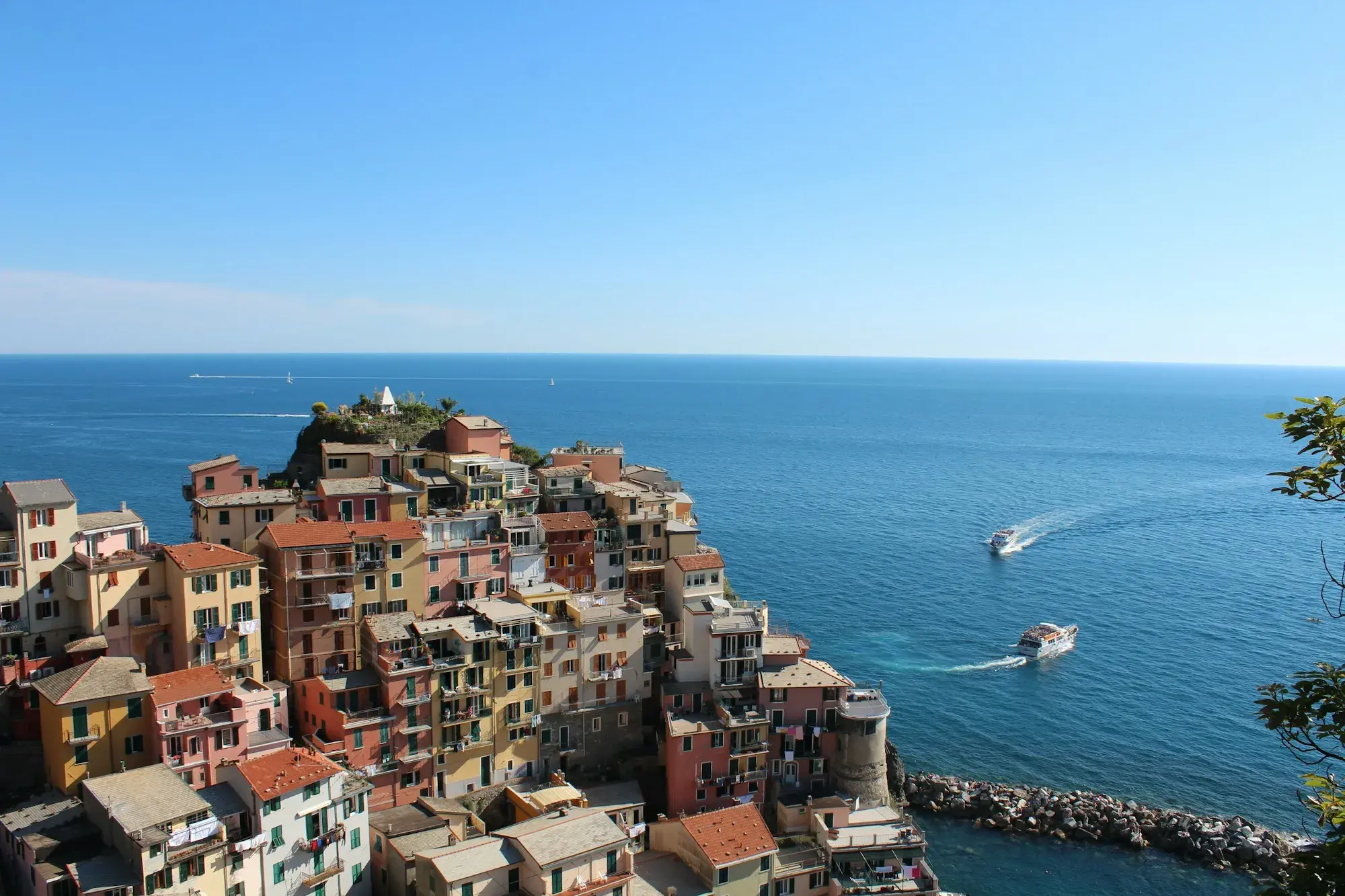 The colourful houses of Manarola on a rocky headland above the blue sea, with a boat passing offshore