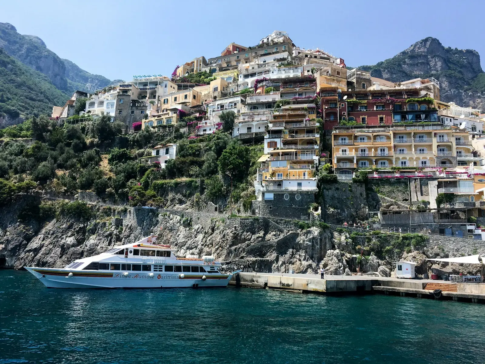 A white passenger ferry moored at the pier below the hillside houses of Positano on the Amalfi Coast