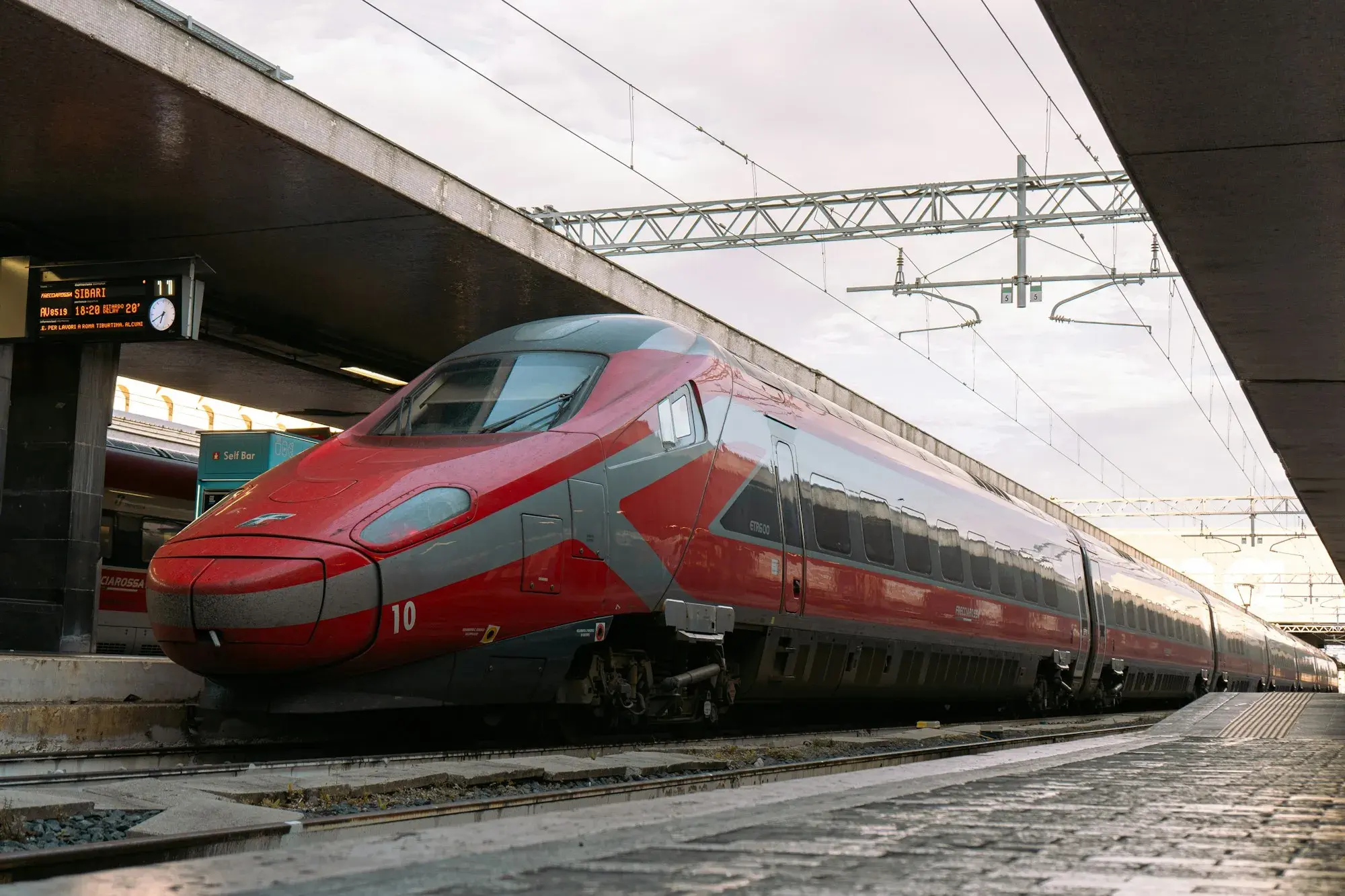 A red high-speed Frecciarossa train standing at a platform under the canopy of Roma Termini station
