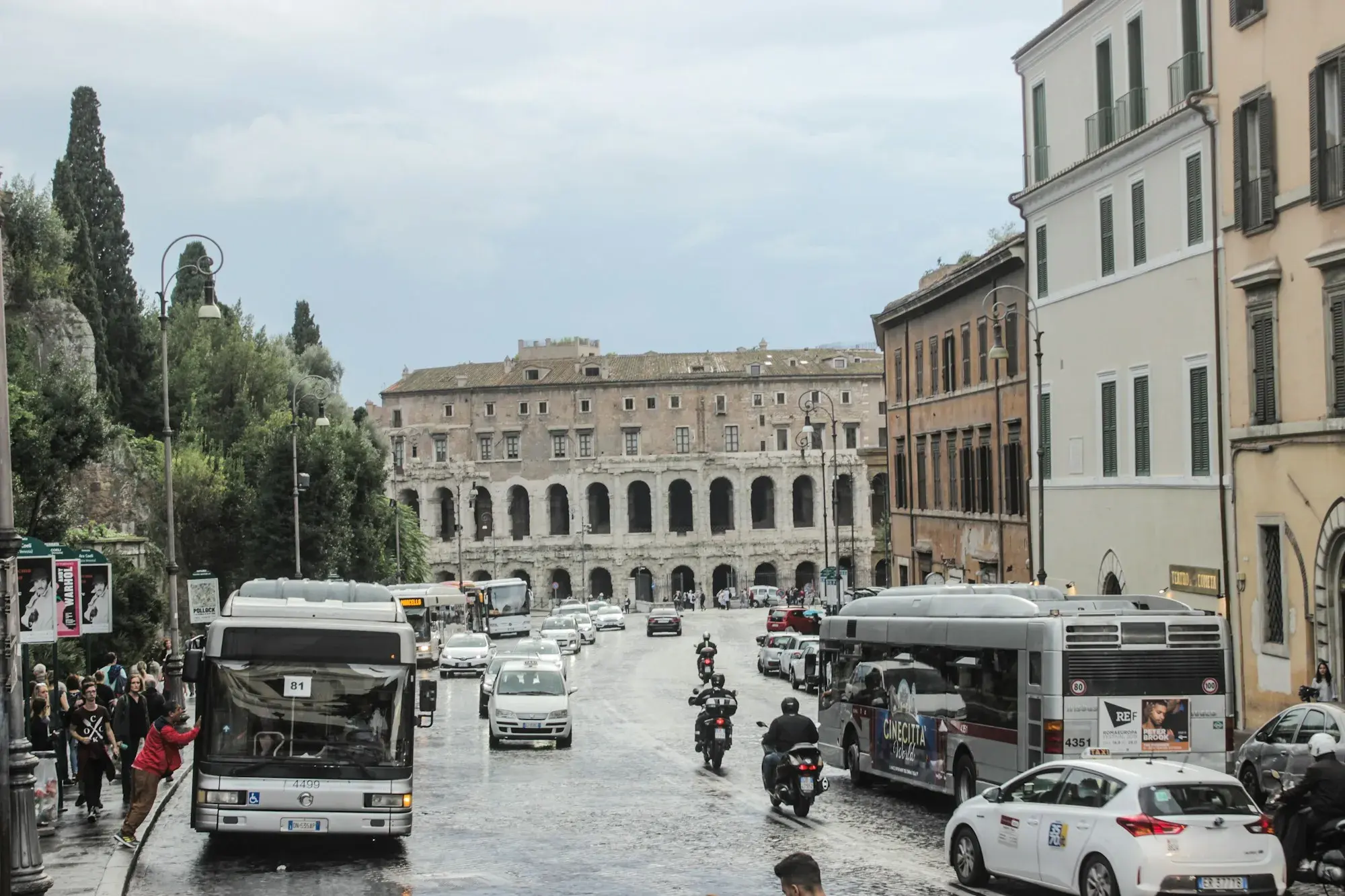 City buses and cars on a wide street near the Theatre of Marcellus in Rome on a cloudy day