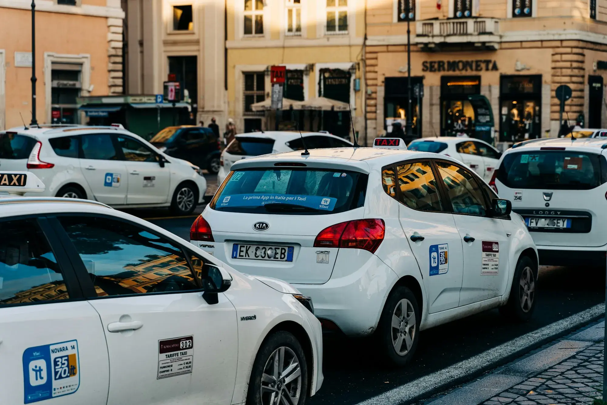 White licensed taxis with roof signs waiting in a line on a street in central Rome