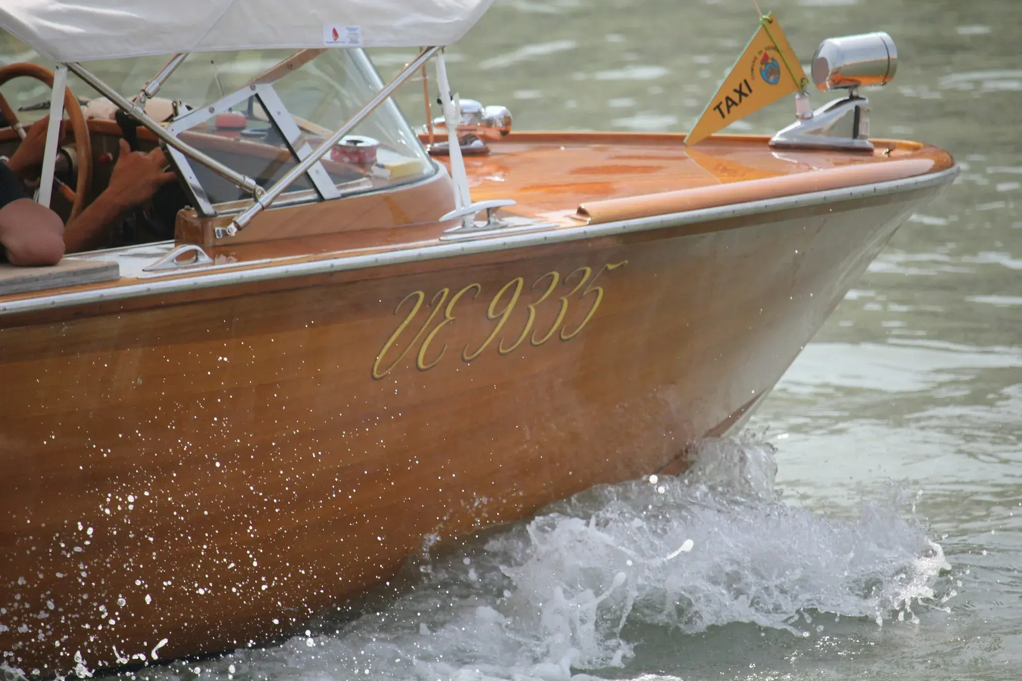 A polished wooden water taxi with a taxi flag speeding across the water in Venice