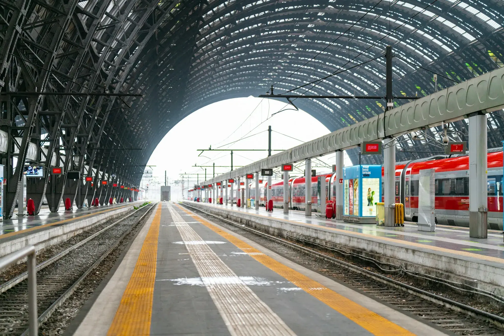 Empty platforms under the arched iron-and-glass roof of Milano Centrale station